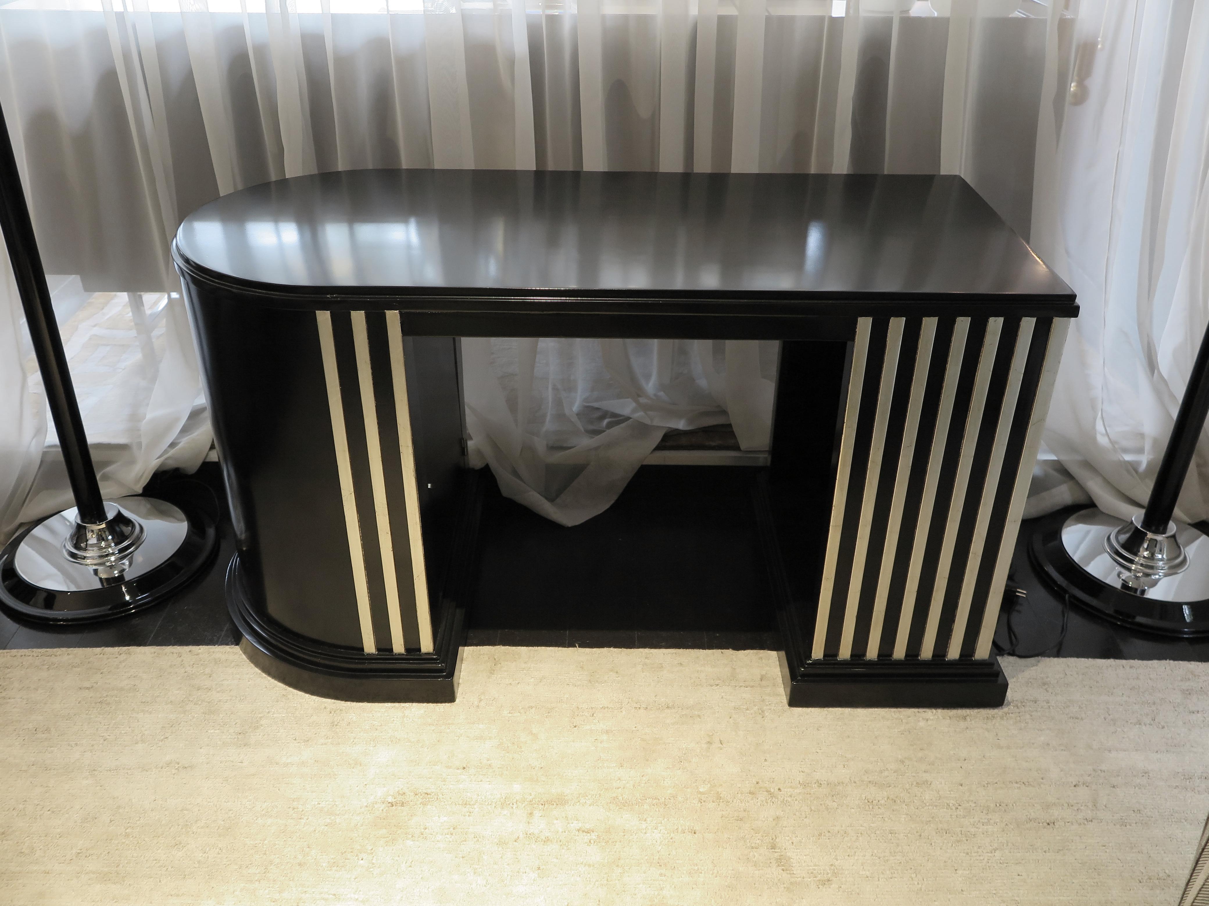 This sleek black lacquer desk features a demilune design. Two pedestal bases one rectangular and one curved. A hidden door compartment fits inside the curved leg. Raised white-gold leaf linear details decorate the desk on both sides.