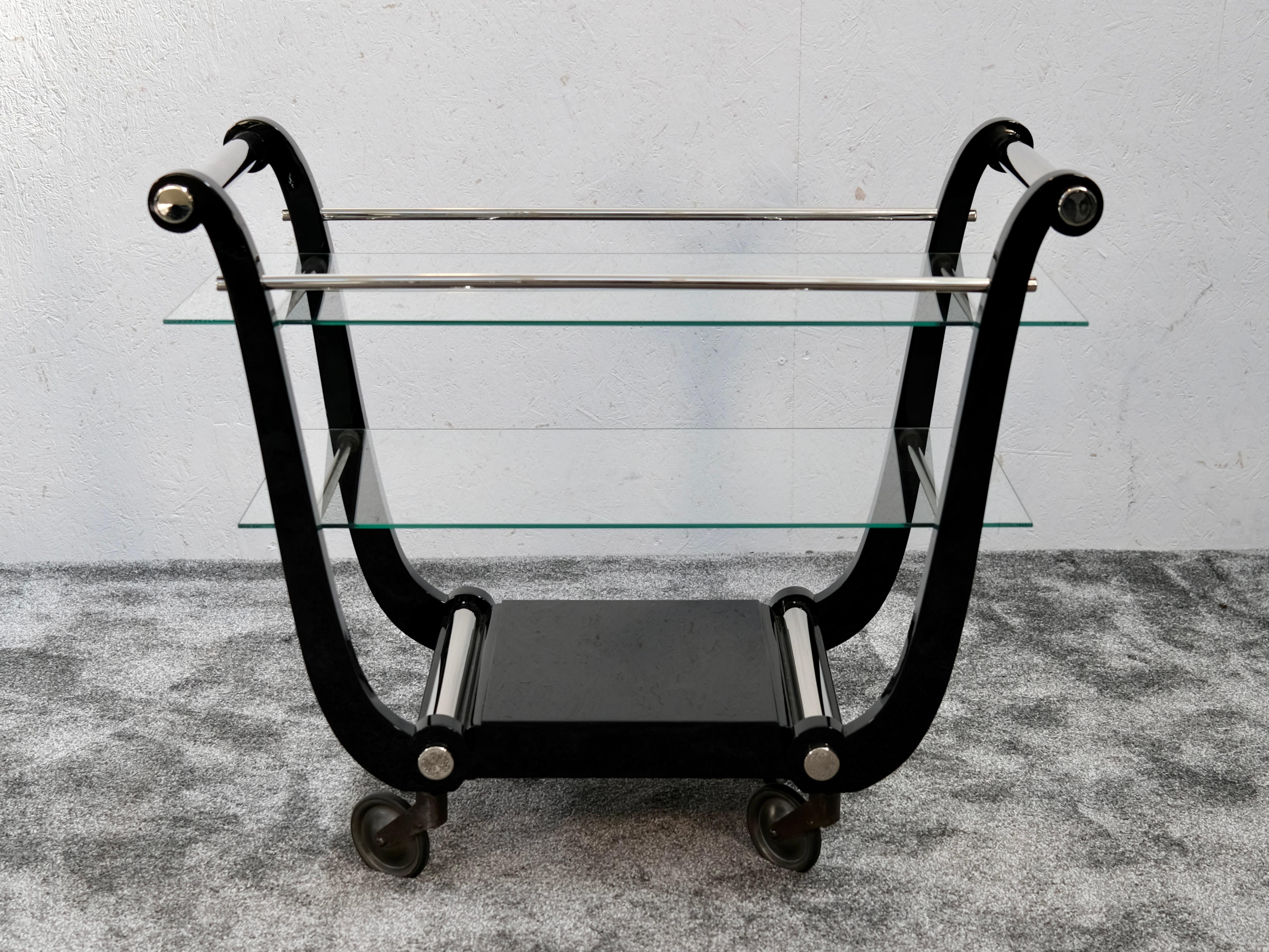 A French Art Deco bar cart in black high-gloss lacquer with chromed details and glass shelves, France, circa 1930. Its distinctive lyre-shaped silhouette is an iconic design gesture of the period — combining elegance, movement, and architectural