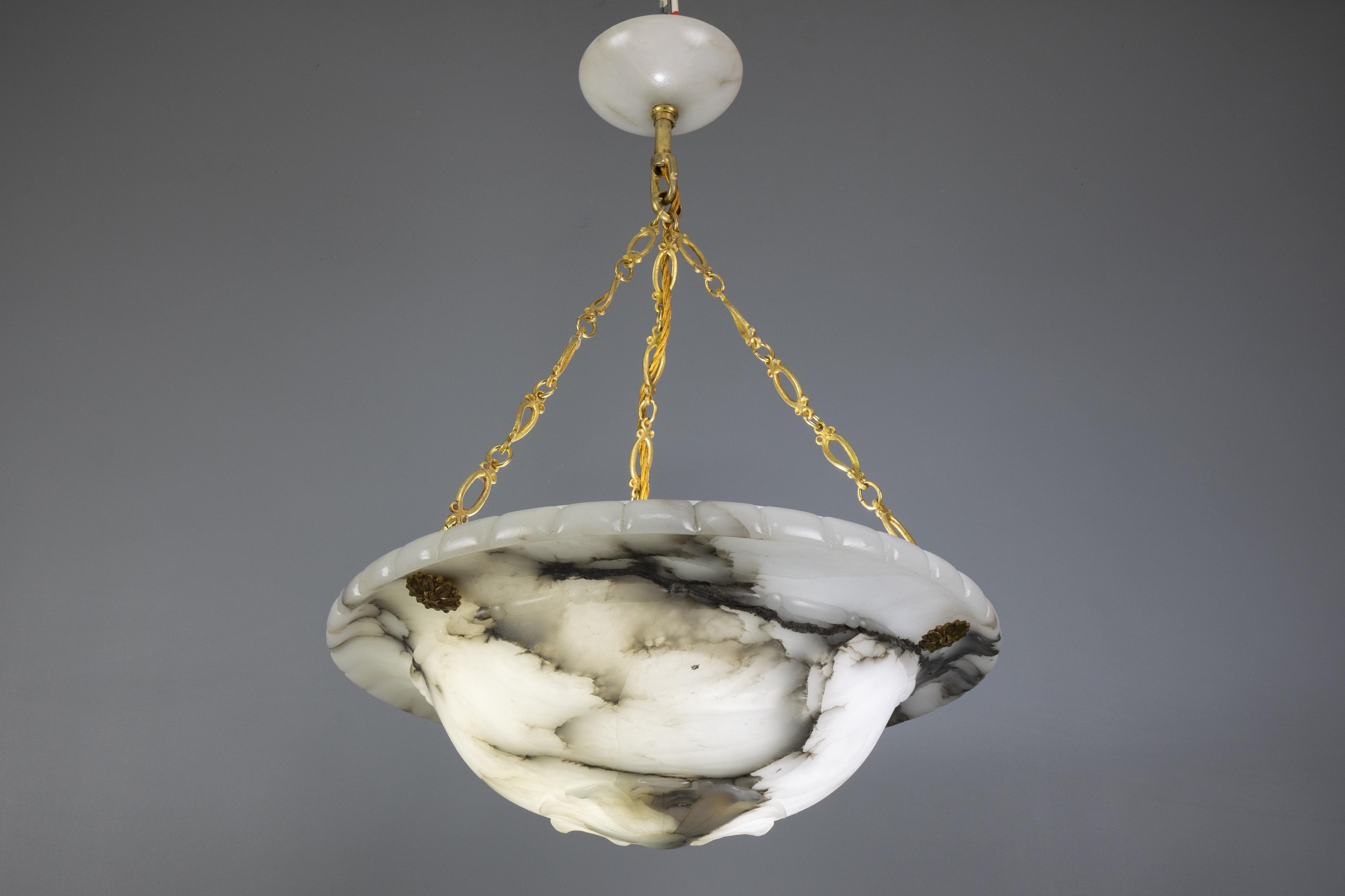 A French Art Deco pendant light fixture from the 1920s made of alabaster with black and greyish veins, featuring a flower motif. 
The alabaster bowl is beautifully shaped and richly veined. It is suspended by three decorative brass chains and a