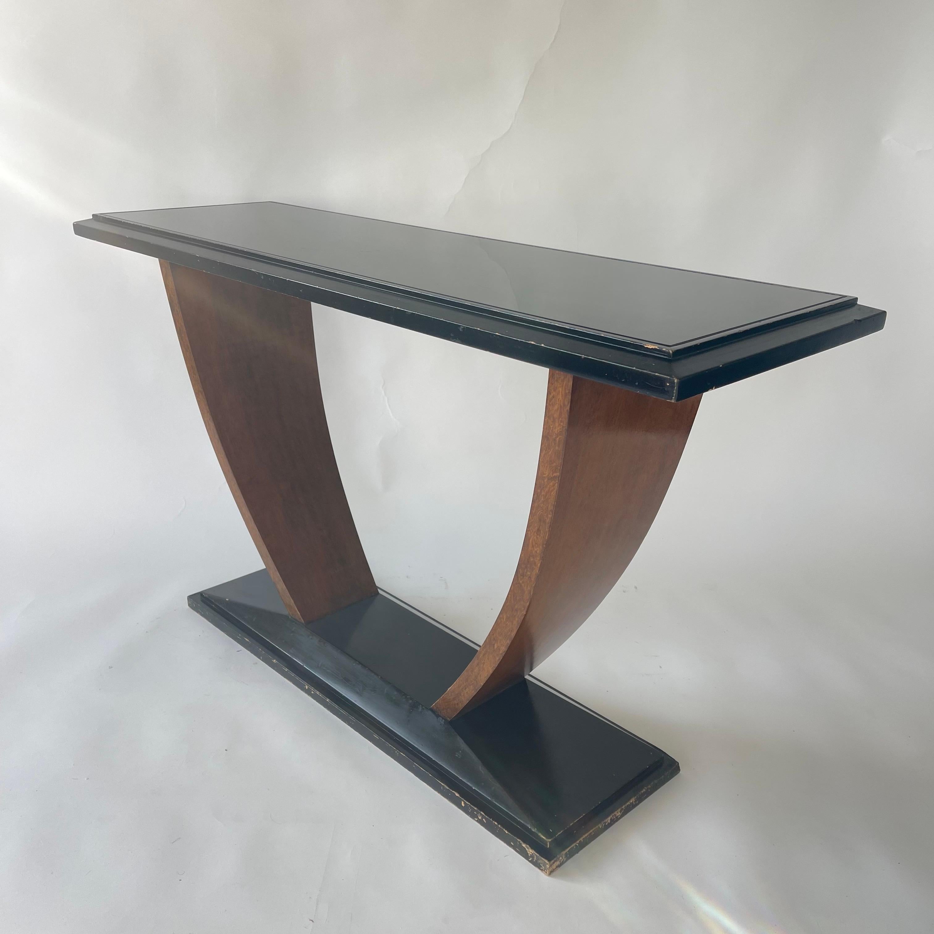 Unique French Art Deco console table rendered in black painted wood supported by a curved walnut base and a black glass inset top.  In the style of Jules Leleu, France, 1930s