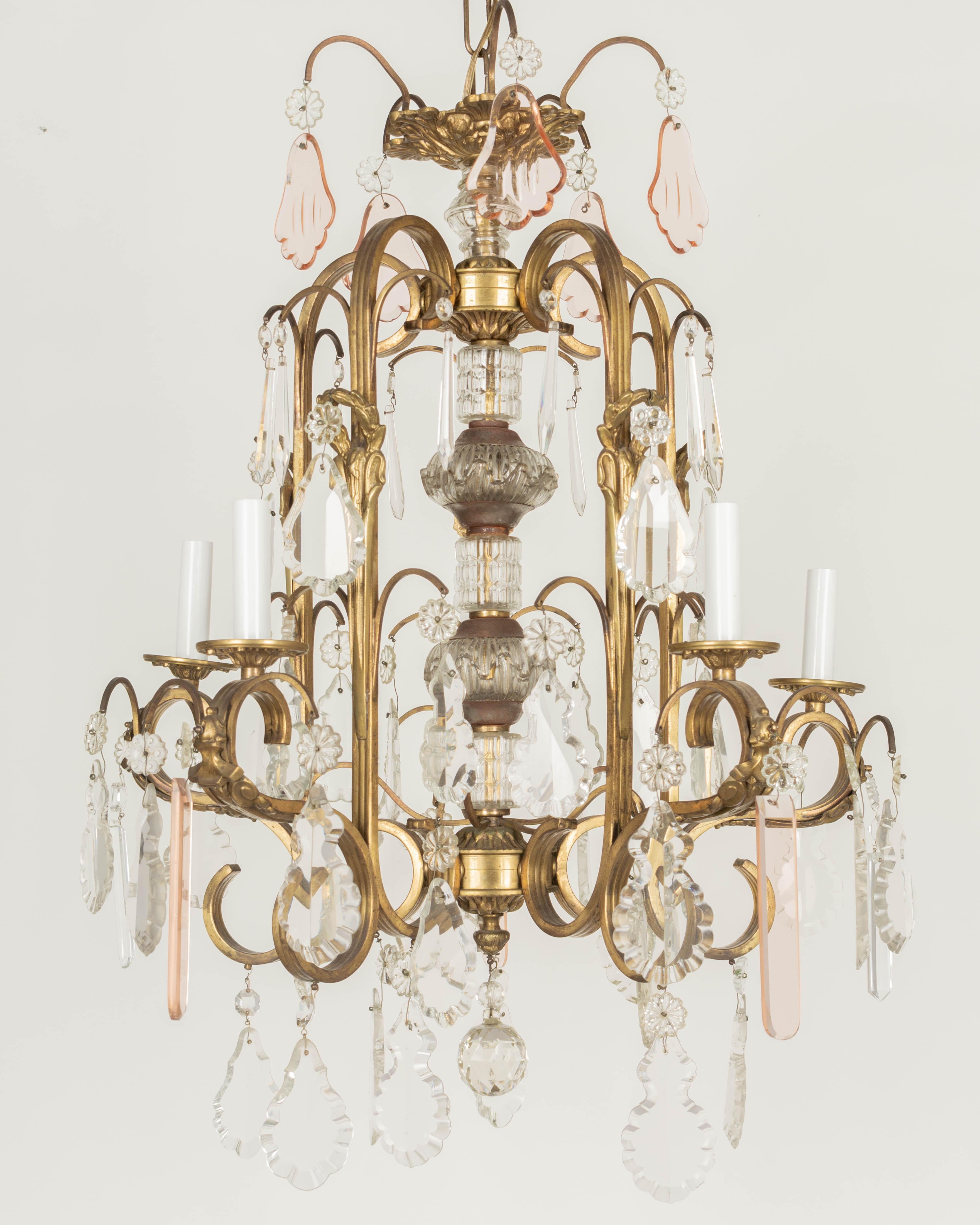 A French Art Deco five-light crystal chandelier. Solid brass flat ribbed tubular frame with scrolled arms with cast brass bobeches and decorative elements. Large center column with cut glass elements. Variety of crystal prisms with rosettes accented
