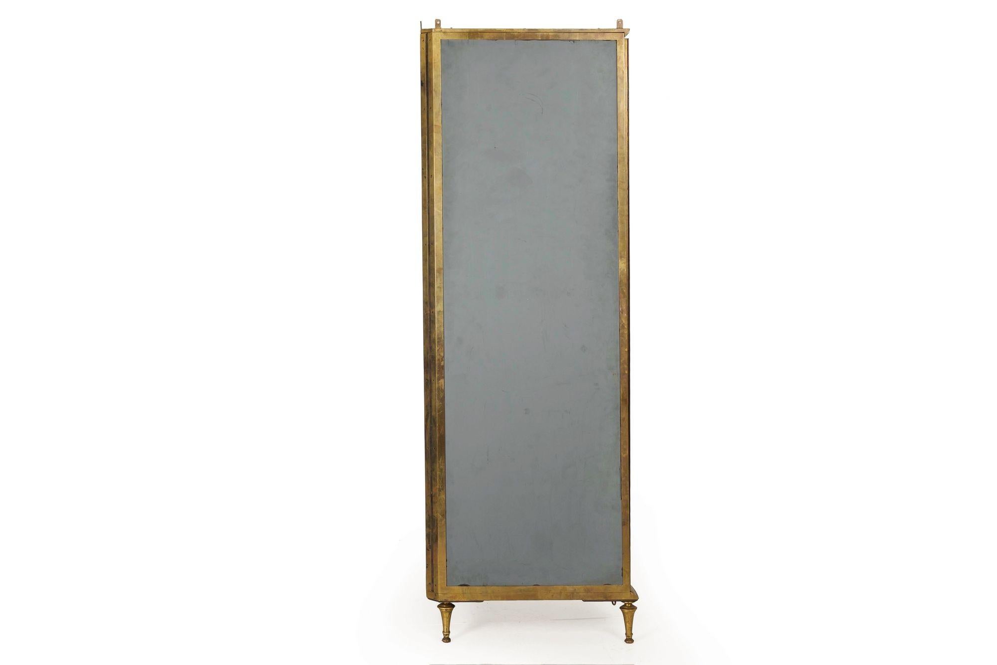 A very finely crafted brass and glass curio cabinet from the second quarter of the 20th century, it features a curved front profile against a triangulated back intended for placement in a corner. The cabinet features four original tabs that allow it