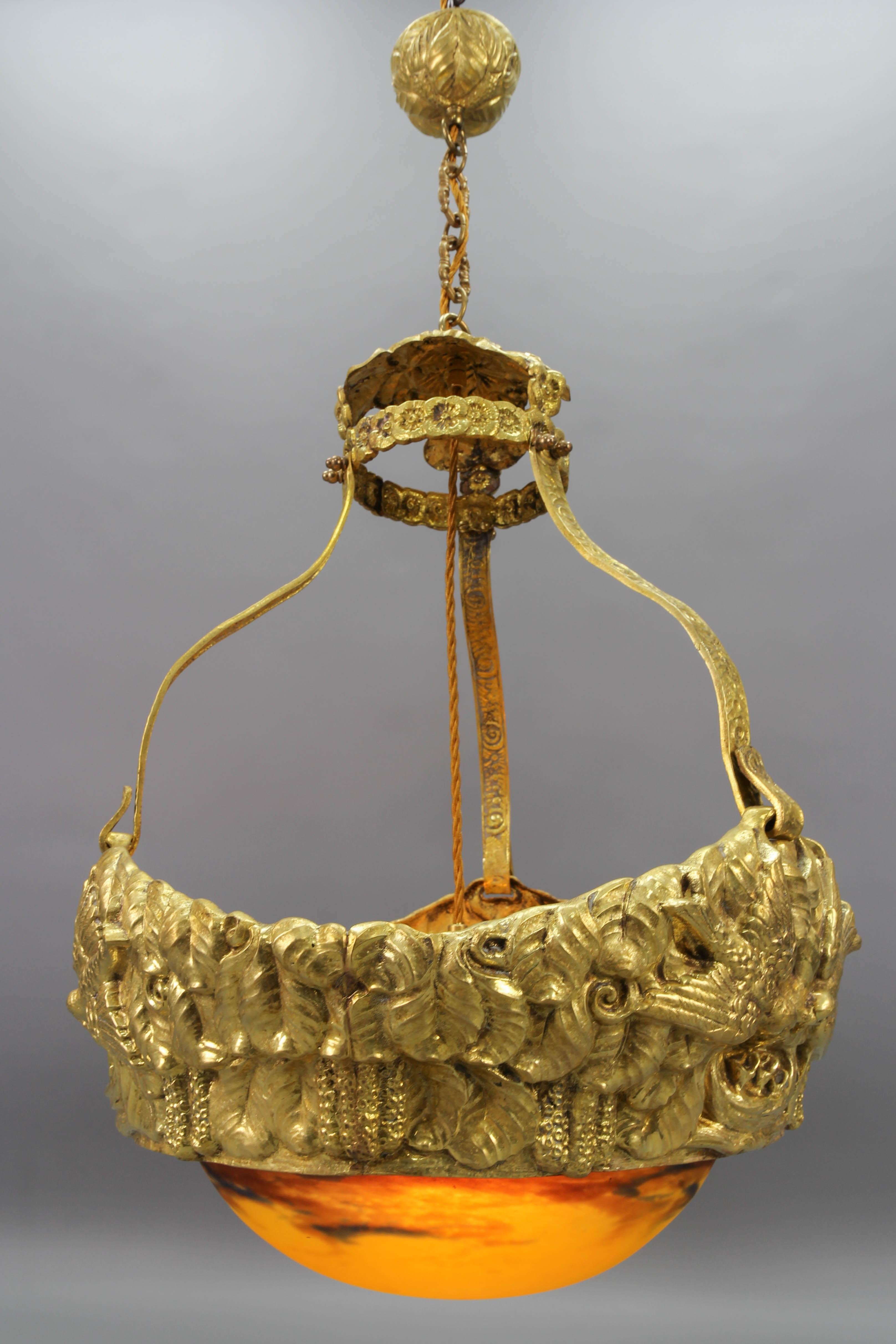 French Art Deco Brass Chandelier Pendant with Pâte de Verre Glass by Degué, from circa the 1930s.
This impressive French Art Deco chandelier features an ornate brass frame in the shape of a nest, on the sides depicting birds and a nest with baby