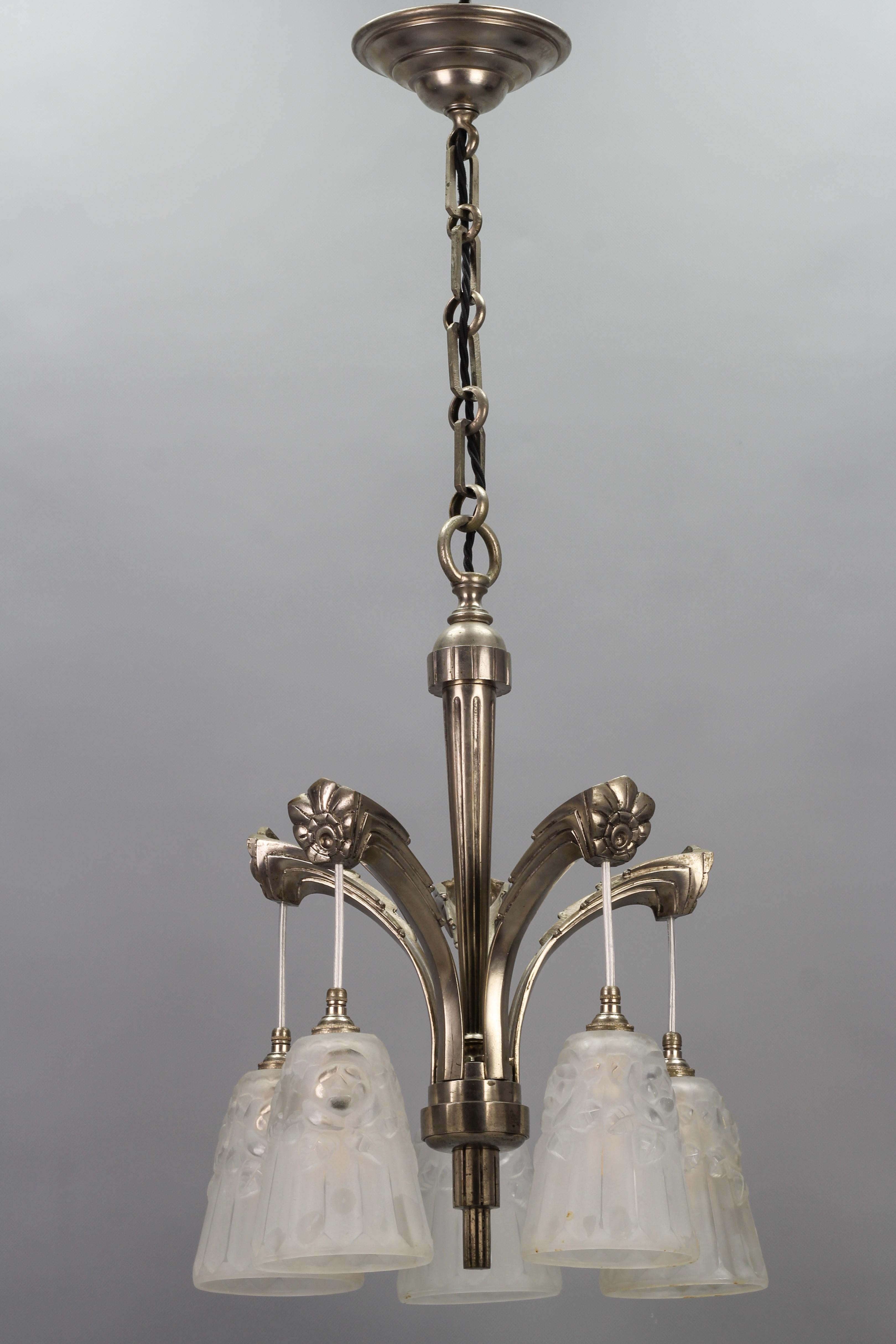 French Art Deco brass five-light chandelier with white glass by Degué, the 1930s.
This beautiful five-light chandelier features an elegant shape nickel-plated brass frame adorned with stylized Art Deco flower ornaments. Five frosted glass white