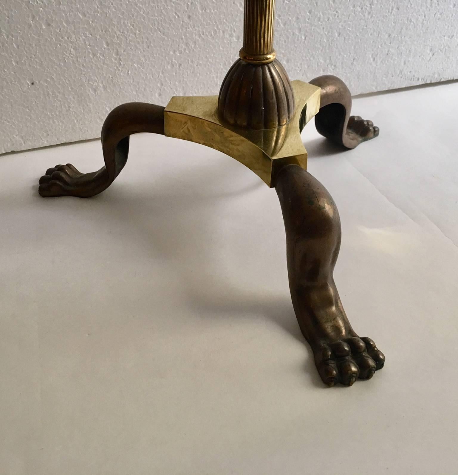 French art deco lamp from 1940, its design is based on the imperial style.
The base has a tripod shape that ends in three lion's claws, made of bronze and brass.
The top ends in three torch-shaped lights, also in bronze and brass with an