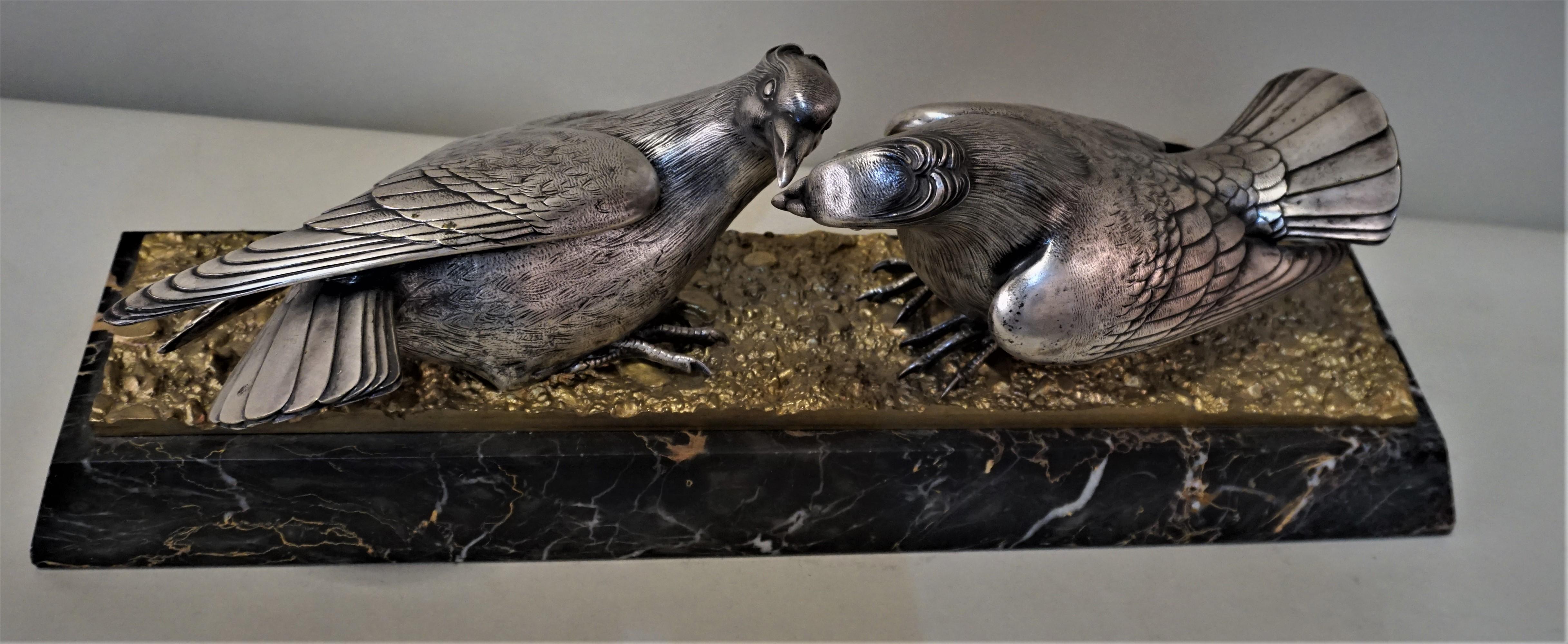 French Art Deco silver sculpture of two birds feeding, standing on golden bronze ground placed on base with multi vein color back marble.