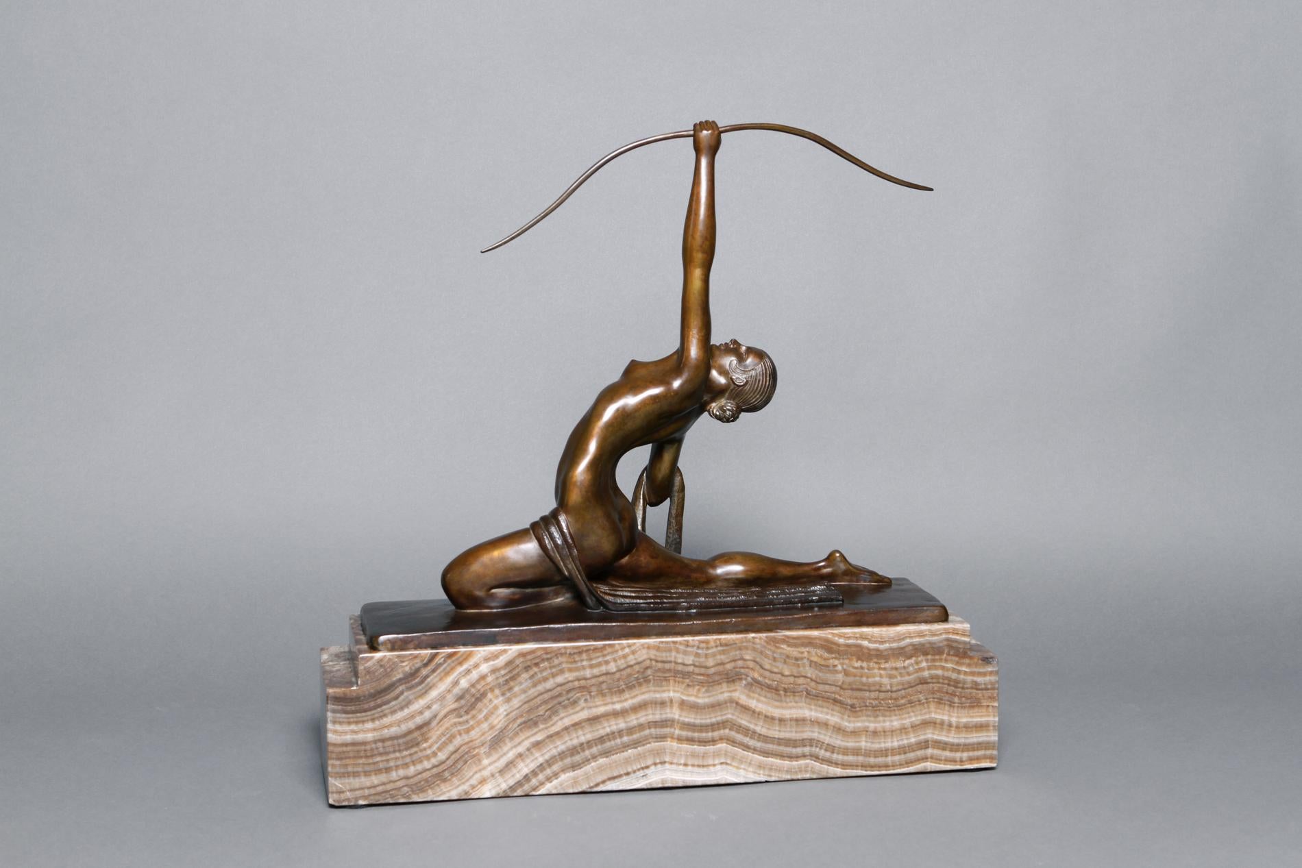 Bronze patinated sculpture by Marcel-André Bouraine representing Diana, female archer. The sculptor choose to represent a naked young woman with length of cloth draped across lap, kneeling backwards and aiming with a bow towards the sky. On a