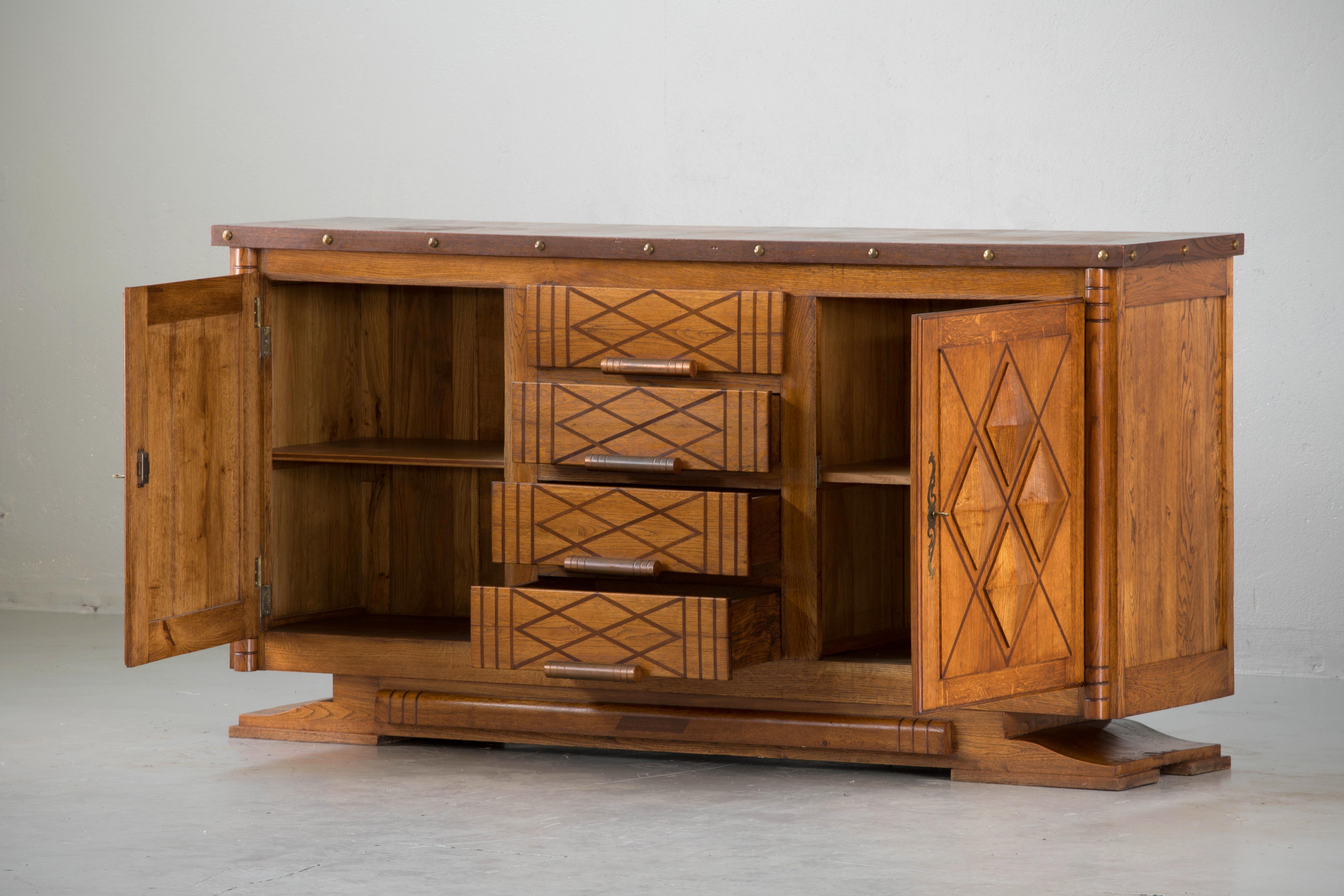 French Art Deco sideboard, Brutalist credenza. The sideboard features stunning oakwood grain. It offers ample storage, with shelve behind two sculpted doors on the sides and dovetailed drawers in the centre. Both sides of the cabinet lock, and two