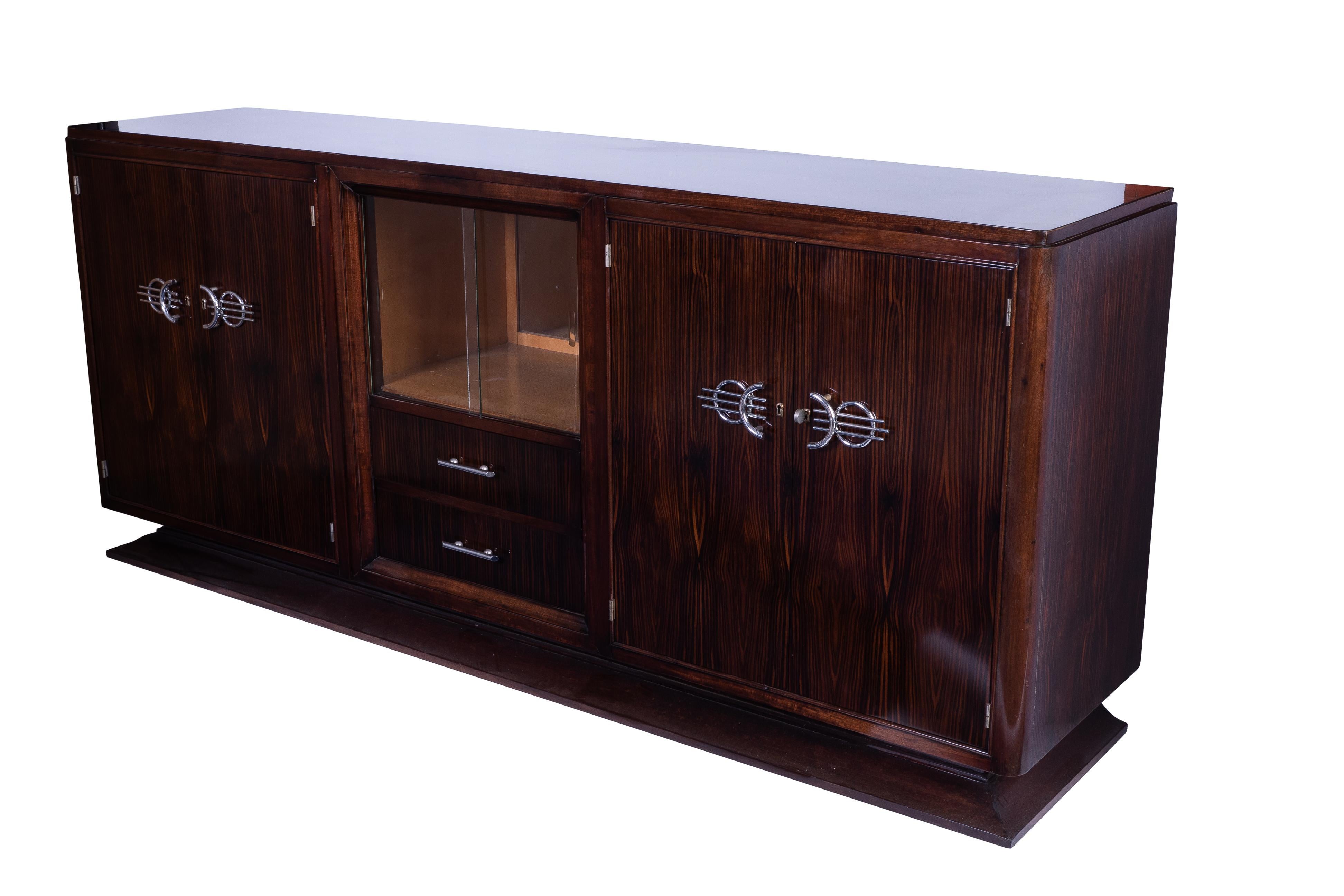 Classic French Art Deco buffet or sideboard in solid Mahogany veneered in Macassar Ebony. The piece has a niche in the center with glass doors and mirror back. Chromed hardware.

Made in France, circa 1925.