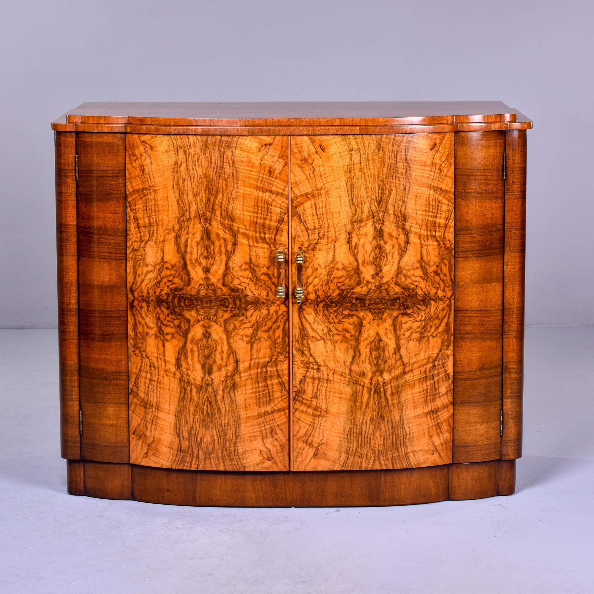 Found in France, this circa 1930s cabinet features beautifully figured burl wood cabinet fronts and a curvy Deco shape. Two hinged doors have lucite and brass hardware. Doors open to a compartment with single fixed interior shelf. Unknown maker. 
 