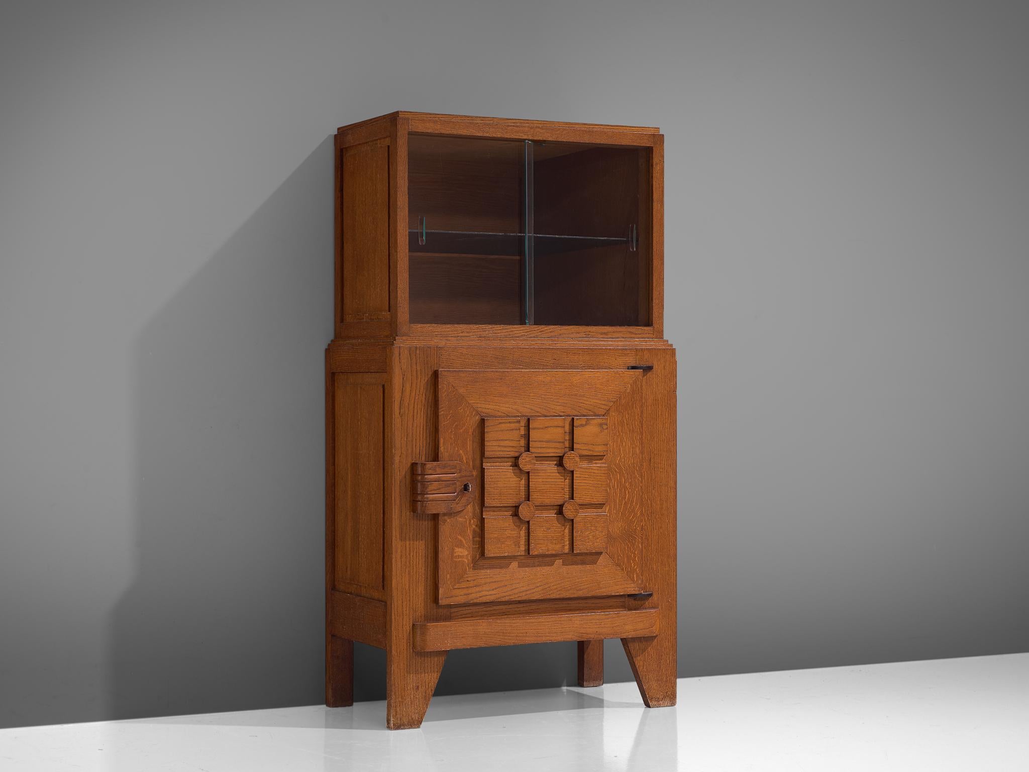 Cabinet, in glass and oak, France, 1950s. 

Robust cabinet in cerused oak with glass vitrine sliding-doors. The high storage part consist of a vitrine part, with one glass shelves. The lower part is a cabinet with one door that has a decorative,