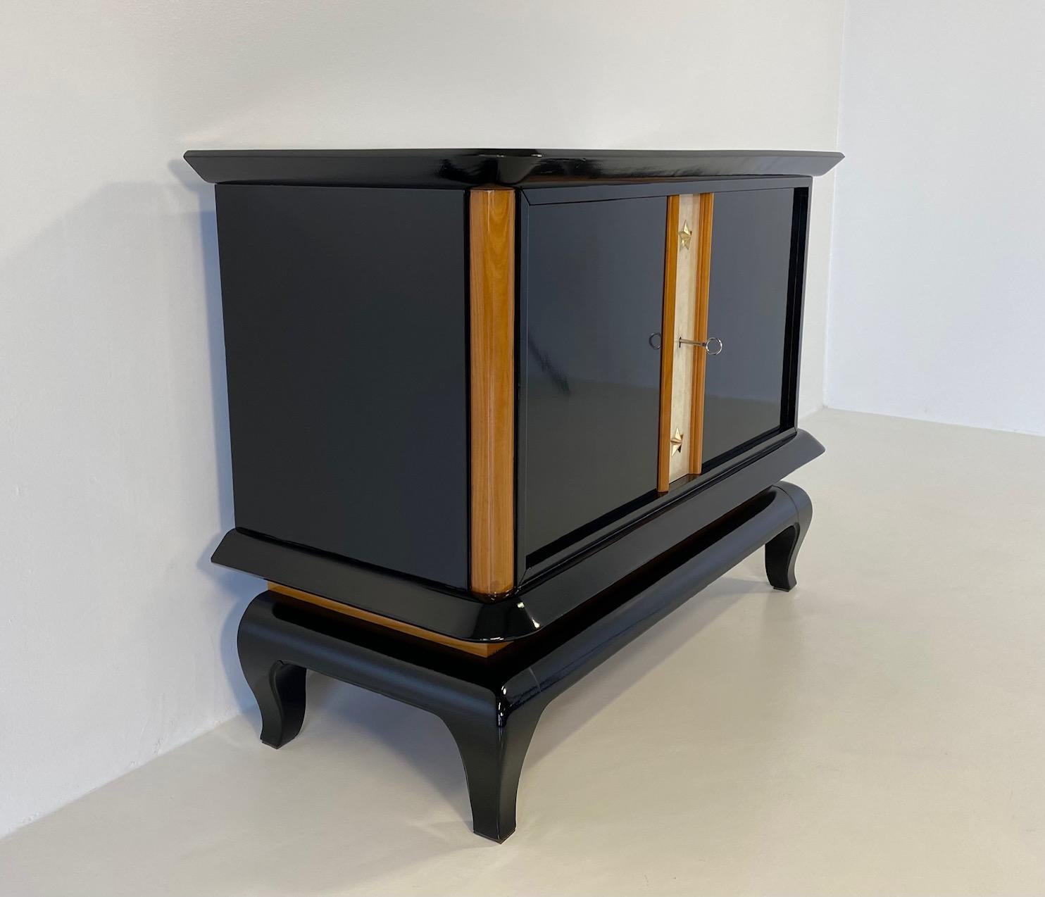 This Art Deco small sideboard was produced in France in the 1940s. 
The structure, the base and the top are black lacquered, some of the frames and the interiors are in maple, the middle part of the front is in parchment, while the decorative stars