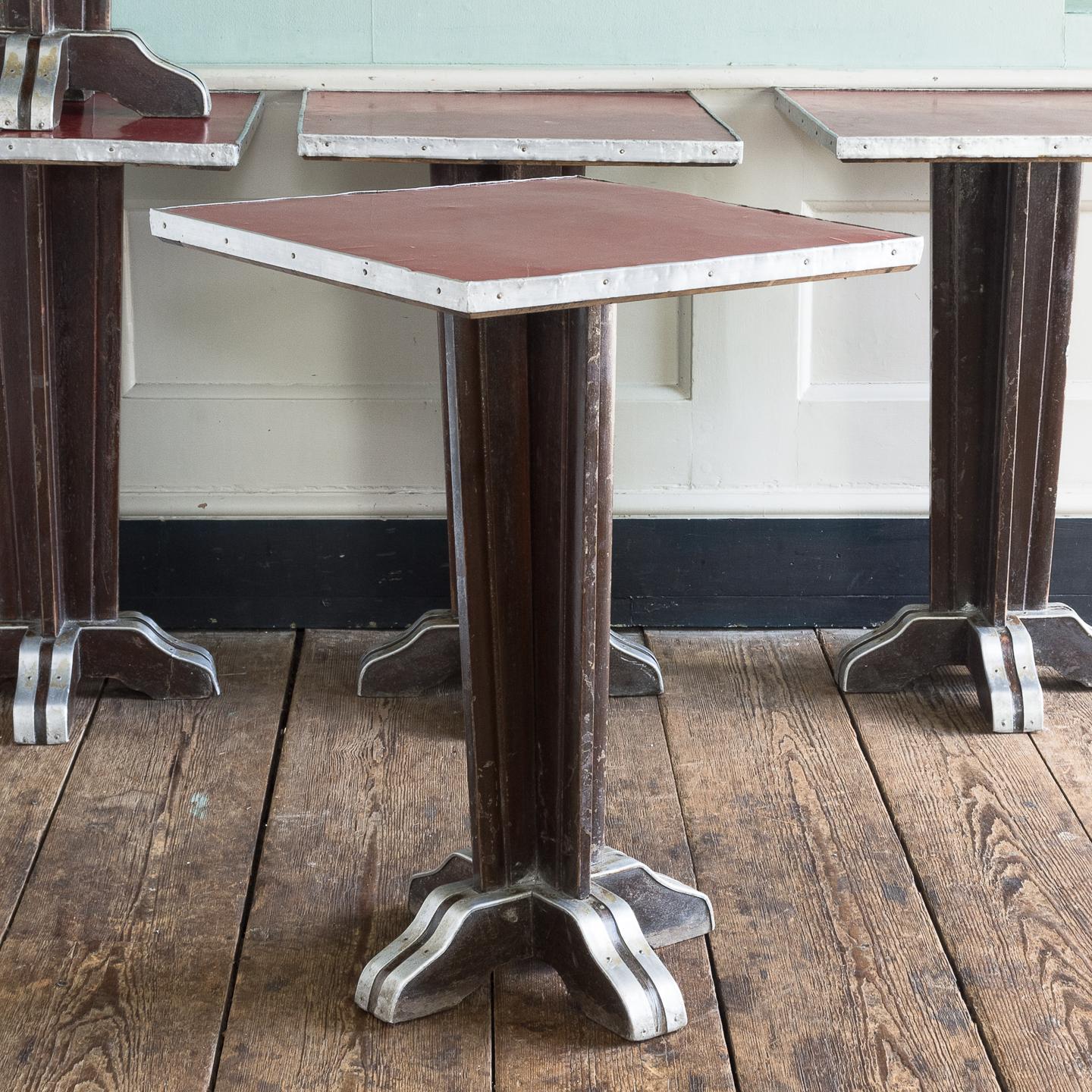 Three French Art Deco cafe tables, the red formica tops with aluminium edging on dark stained beechwood bases, with further aluminium details, in good usable condition, with expected marks and obvious wear.