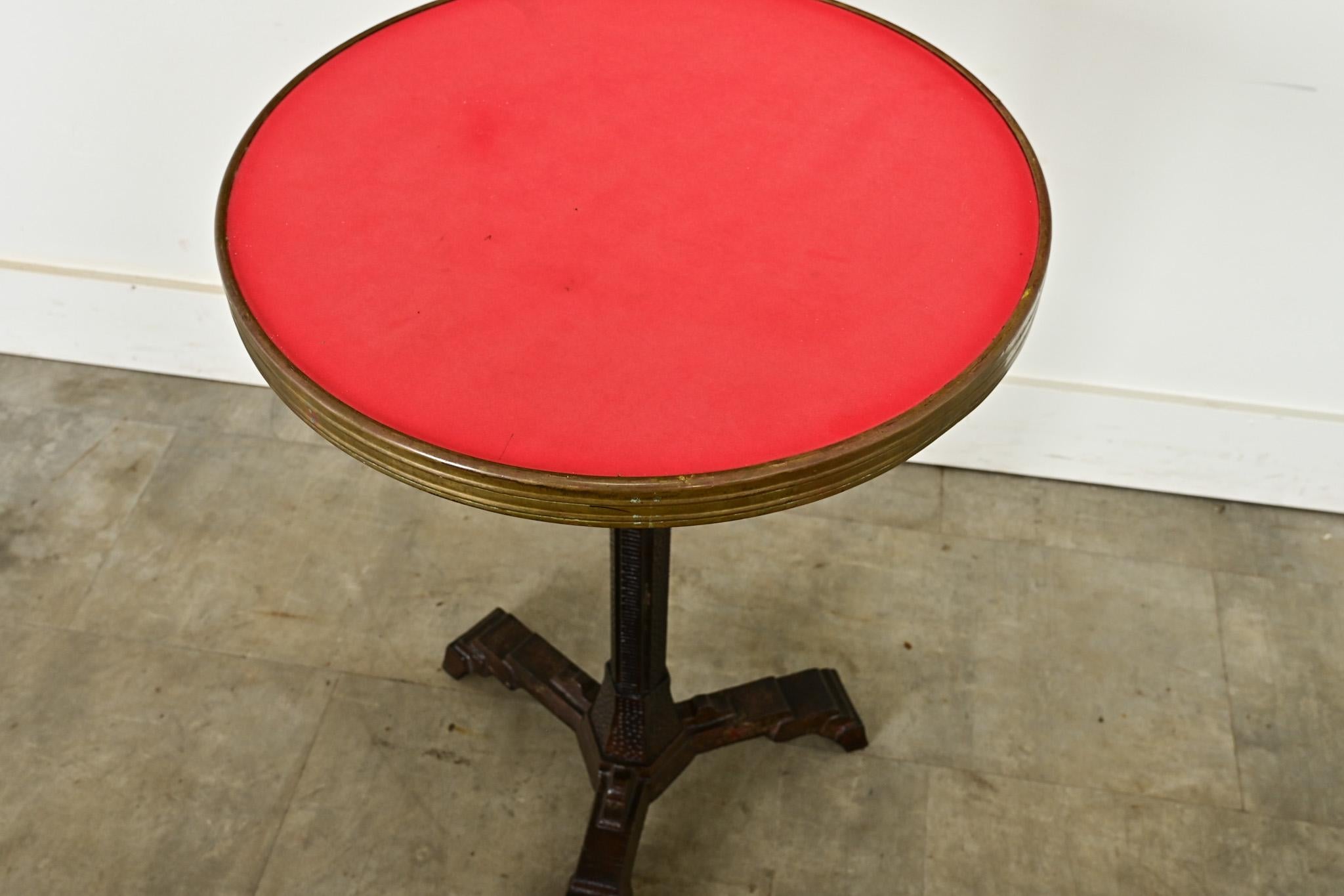 An exciting little bistro, or drinks table from France of the Art Deco period. Within a brass belt around the table top, sits a very practical Formica surface in cardinal red. The cast iron pedestal is hexagonal in shape, covered with repetitive