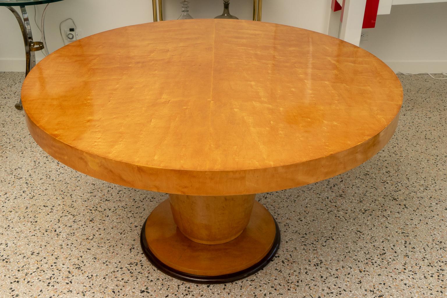 This stylish and chic French Art Deco center table was acquired from a Palm Beach estate and it dates to the 1930s-1940s. The piece is fabricated with sycamore wood veneers in a warm, golden coloration with a dark brown accent color on the pedestal