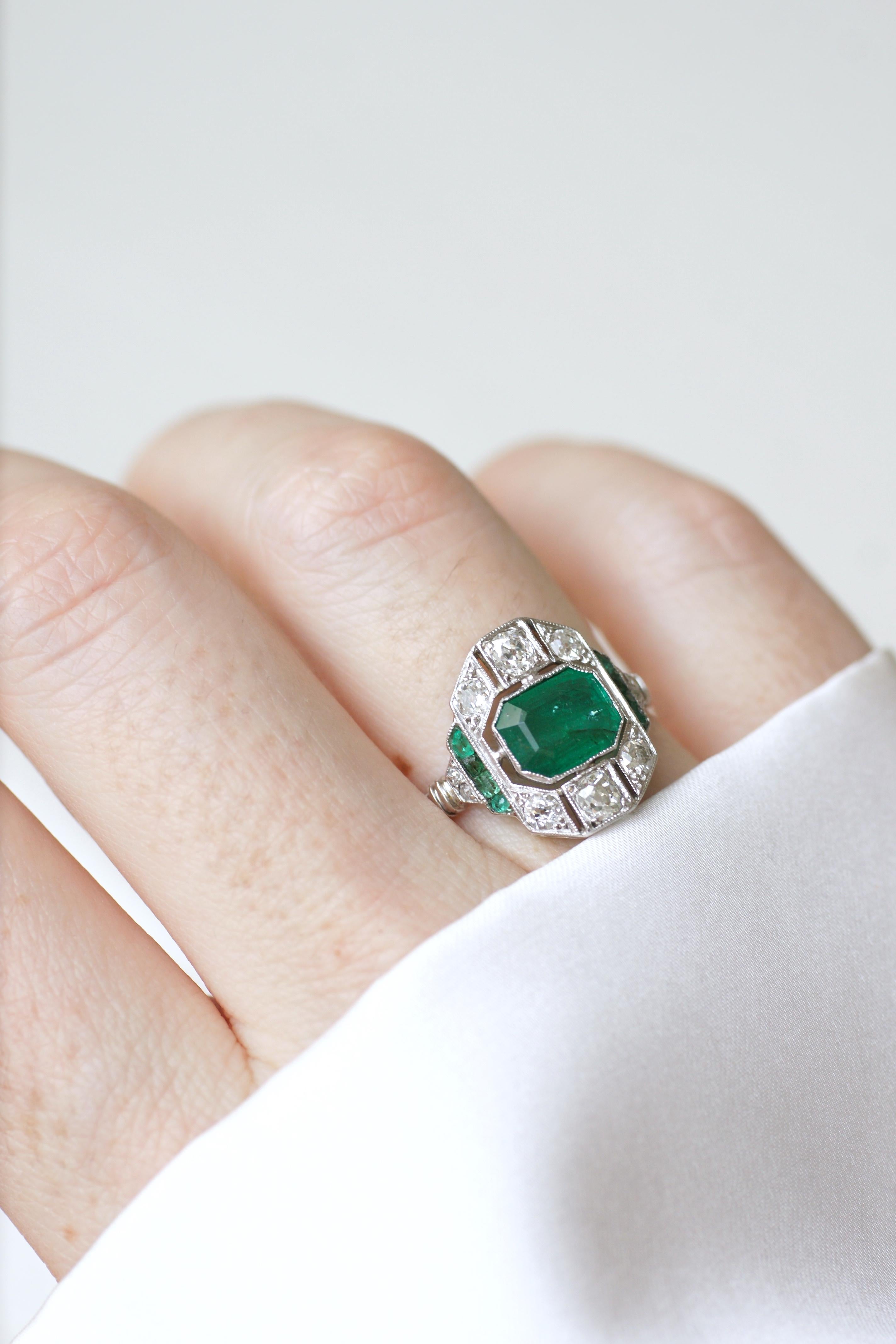 Art Deco ring in 18Kt white gold (hallmark: eagle) set with an emerald cut emerald weighing approximately 1.30 Cts, surrounded with old cut diamond which total weight is apx 0.65 Ct, and square cut emeralds, which total weight is apx