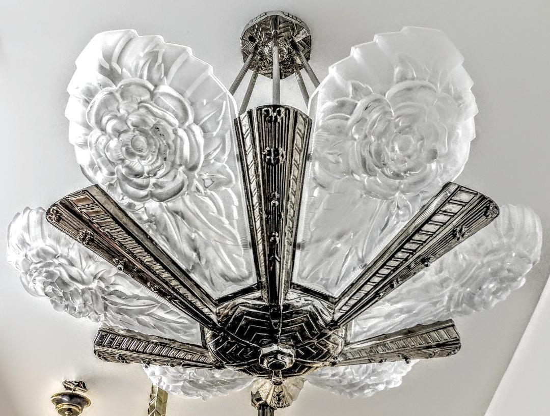 A French Art Deco chandelier with six grand clear frosted molded shades in great condition. Each shade is signed by the French artist Degue. Flower motif polished details mounted on a matching silvered bronze streamlined frame. Rewired to U.S.