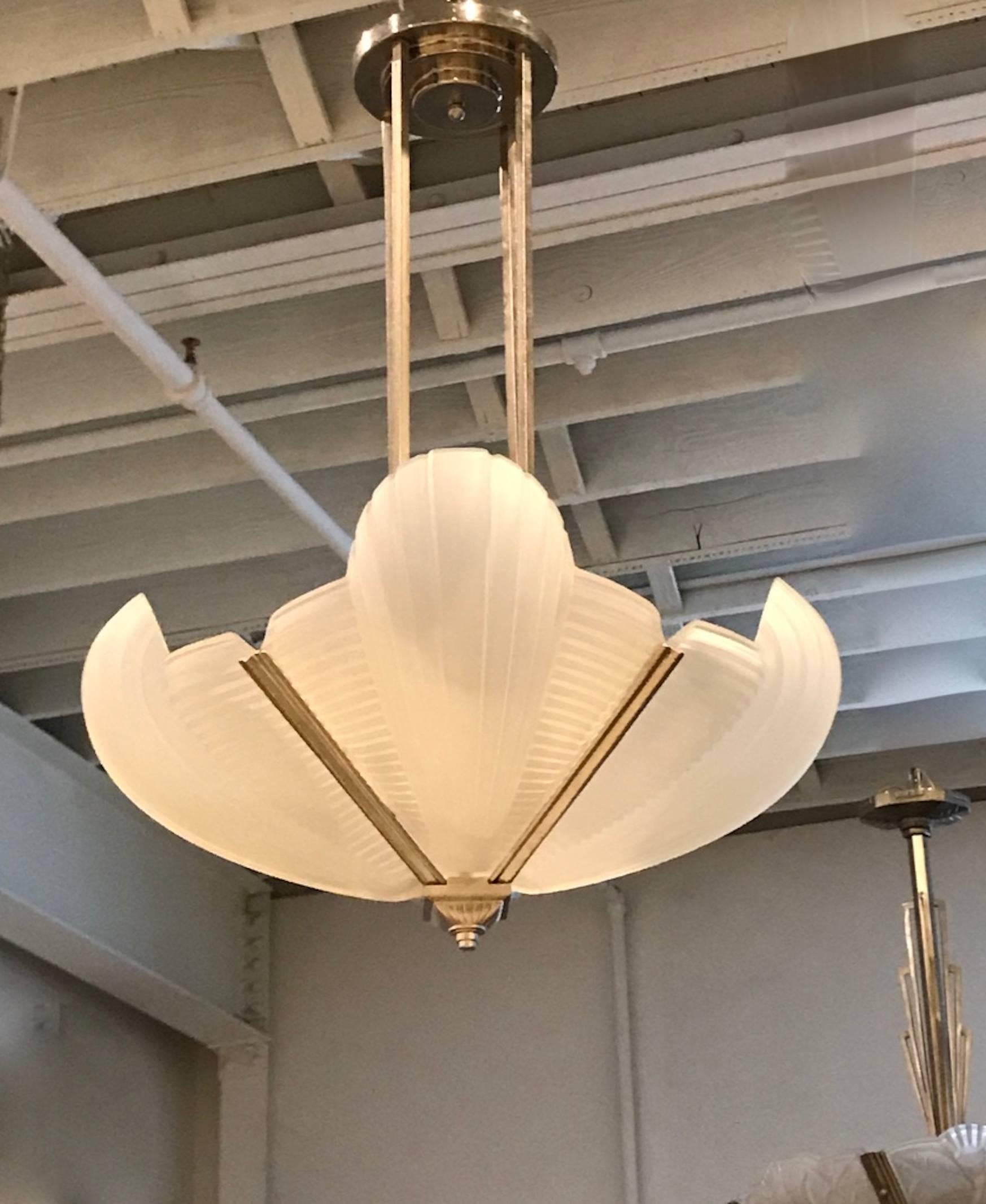 Stunning French Art Deco chandelier by Atelier Petitot. Having four clear frosted glass skyscraper panels with vertical and horizontal ribbed design details. Shades rests on a geometric deco design frame in silvered nickel finish. Having a beautiful