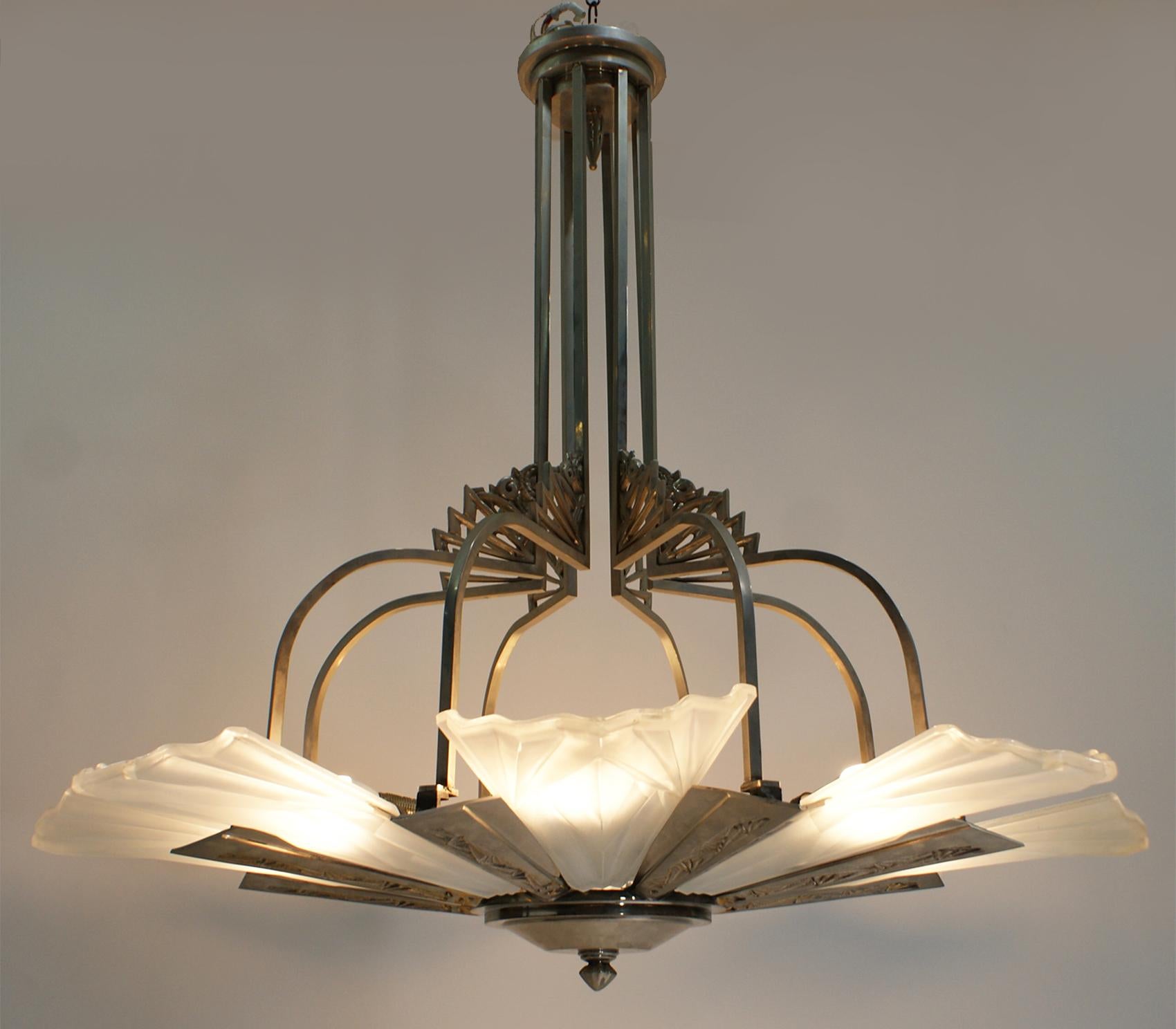 A large gorgeous French Art Deco chandelier signed “Degué” with eight big sided glass shades. Have raised geometric motif design. Each shade is signed by the artist “Degué”. Held by a matching original design in silvered bronze support frame with