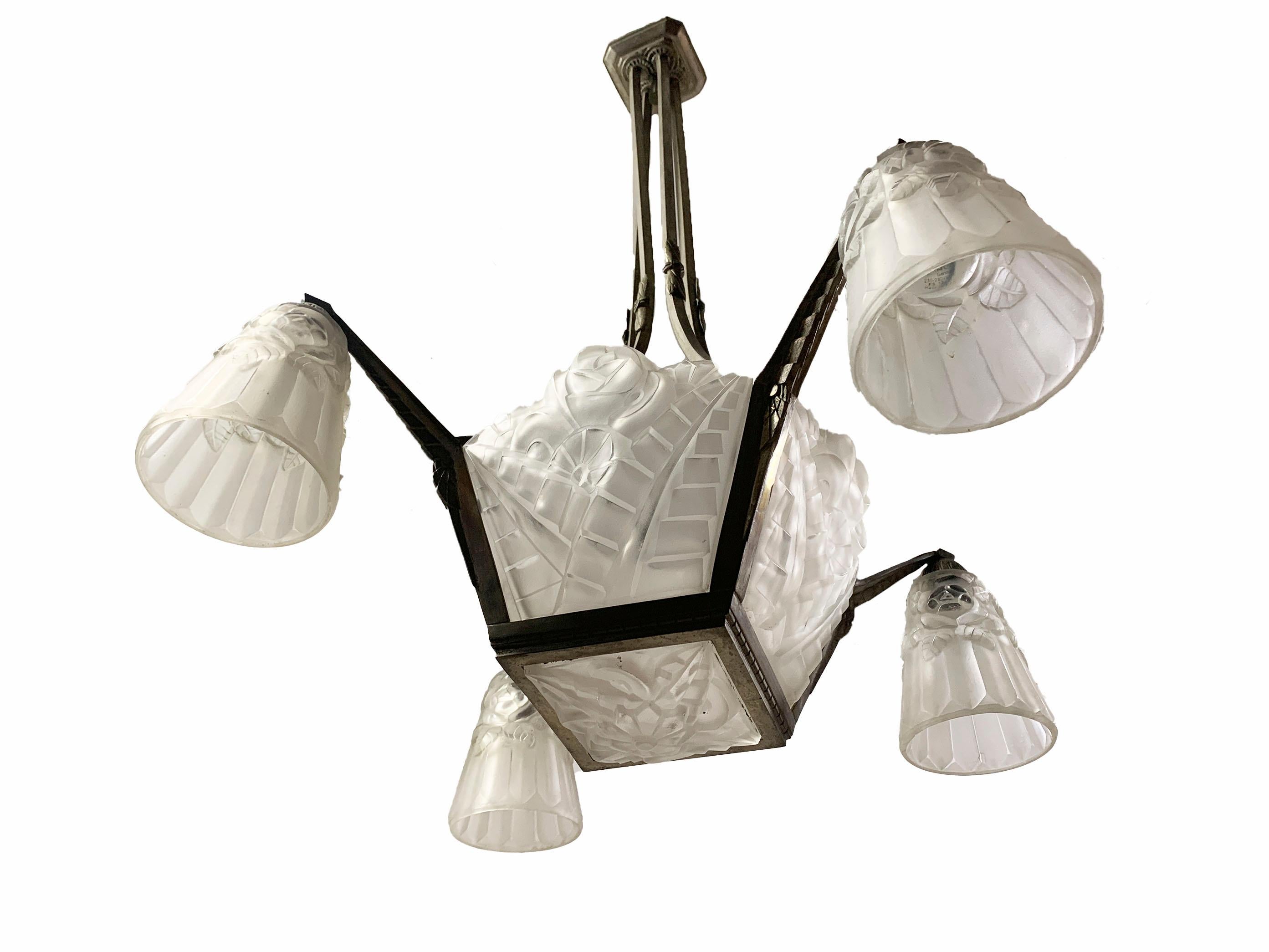 Eccezionale esempio di design Art Déco francese, questo lampadario presenta cinque paralumi in vetro smerigliato stampato, quattro paralumi a tulipano pendenti, tutti firmati Degué, e un corpo centrale geometrico in bronzo con finitura in nichel. La