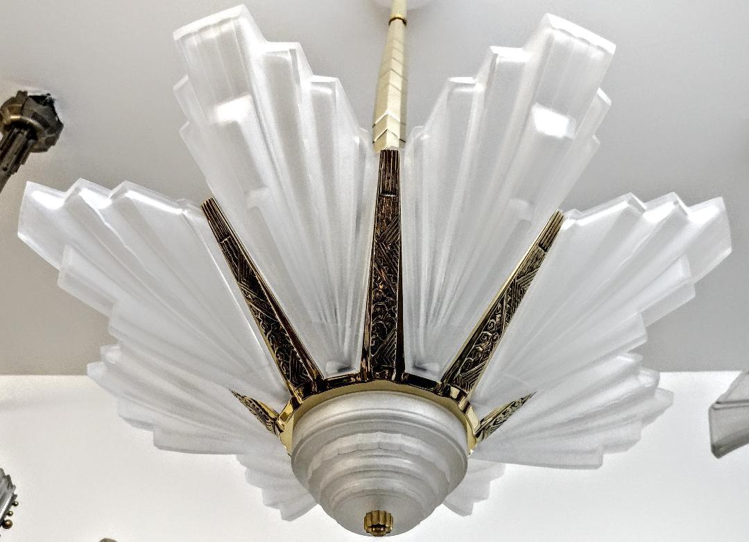 A stunning French Art Deco chandelier by the French Artist Sabino. Eight glass panels with a center coupe signed SABINO FRANCE in clear frosted molded glass with geometric details. Supported by matching streamlined polish bronze mounting enhanced by