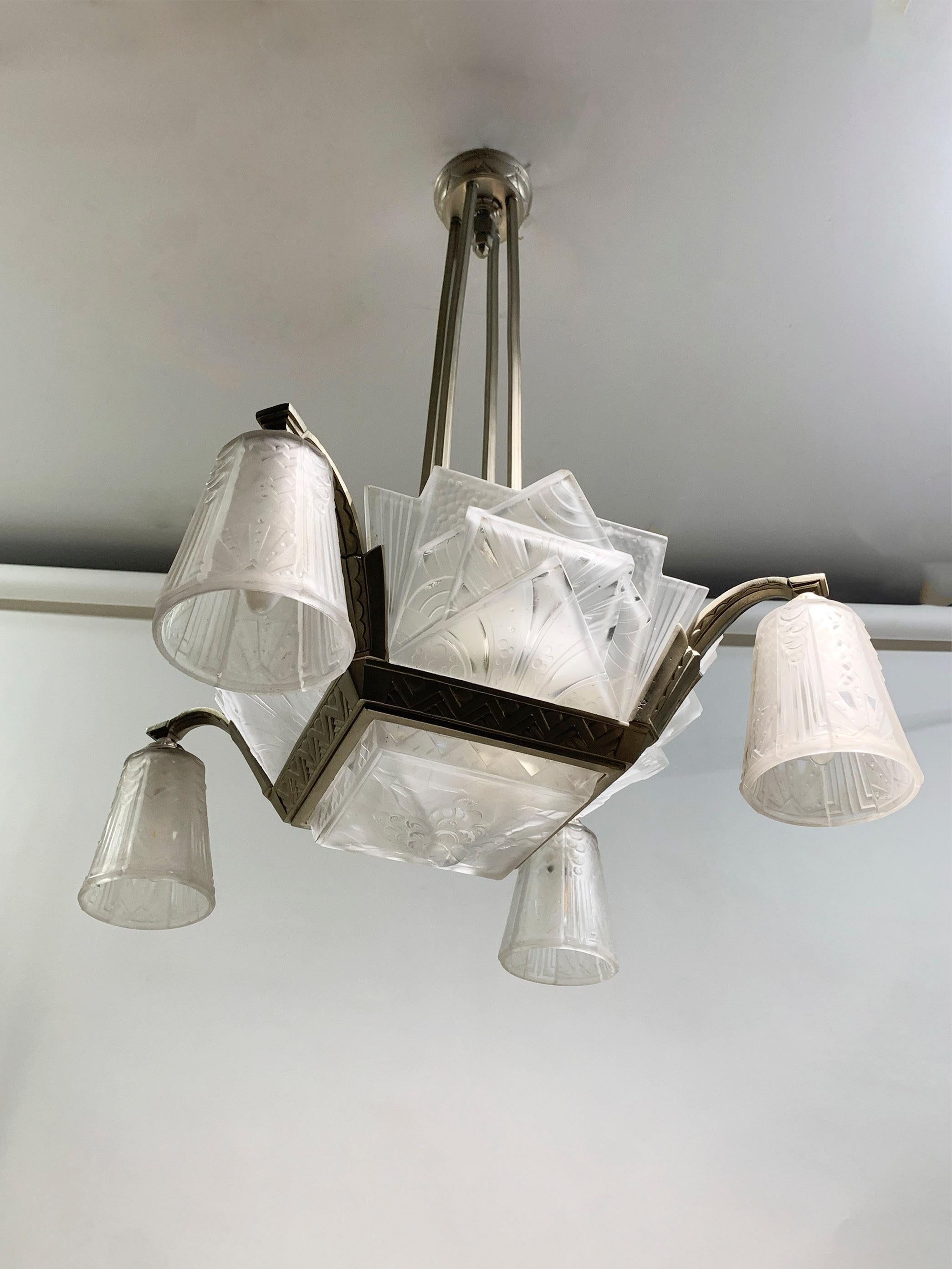 This striking Art Deco chandelier by Muller Frères, circa 1930s, features five press molded frosted glass shades with geometric and stylized floral motifs arranged in a stepped formation, complemented by four elegantly curved arms each holding a