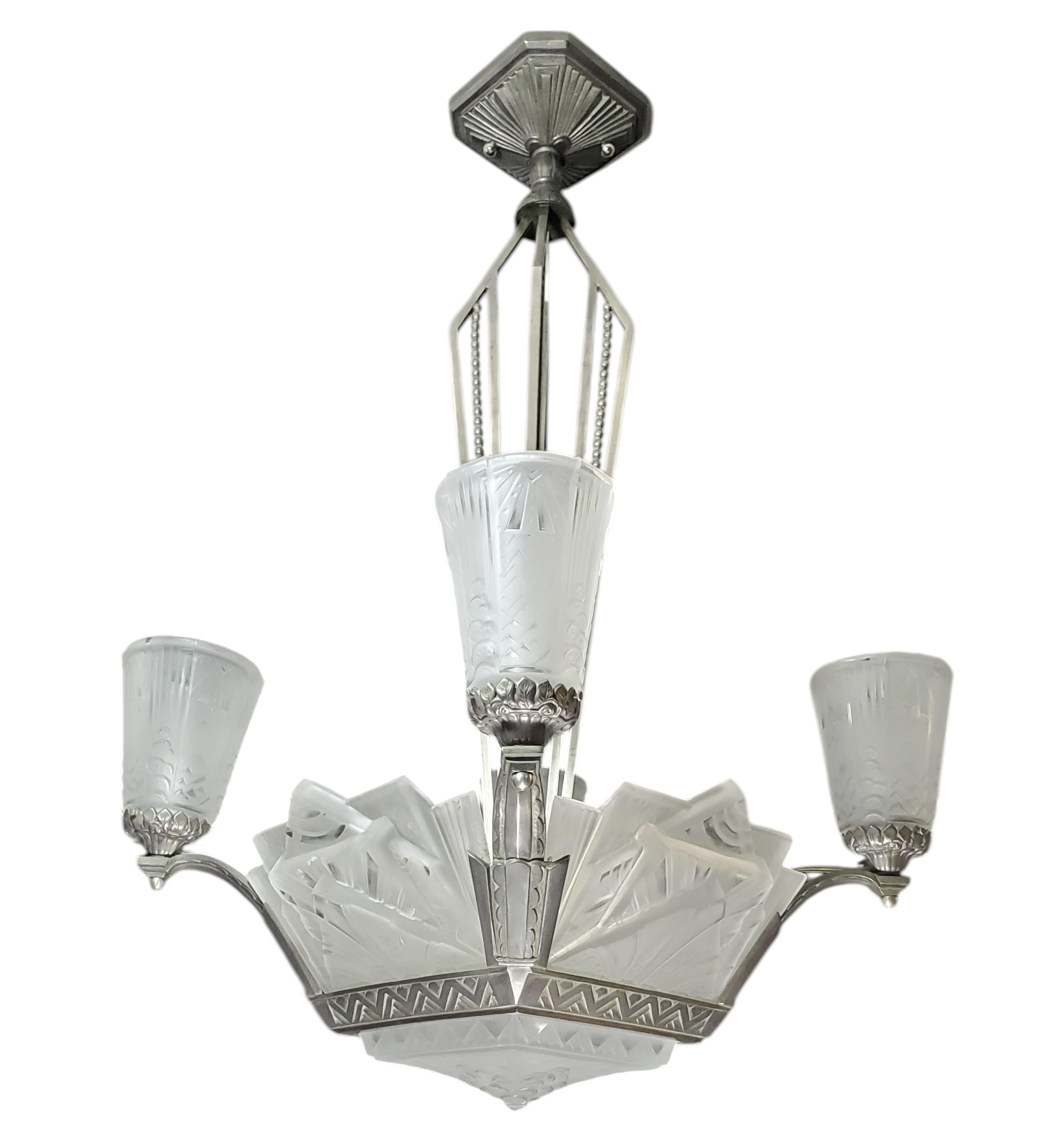 
An exceptional example of French Art Deco lighting, this chandelier signed by Muller Frères features a central arrangement of five molded frosted art glass shades with architecturally stylized geometric motifs. The shades are stepped in elevation