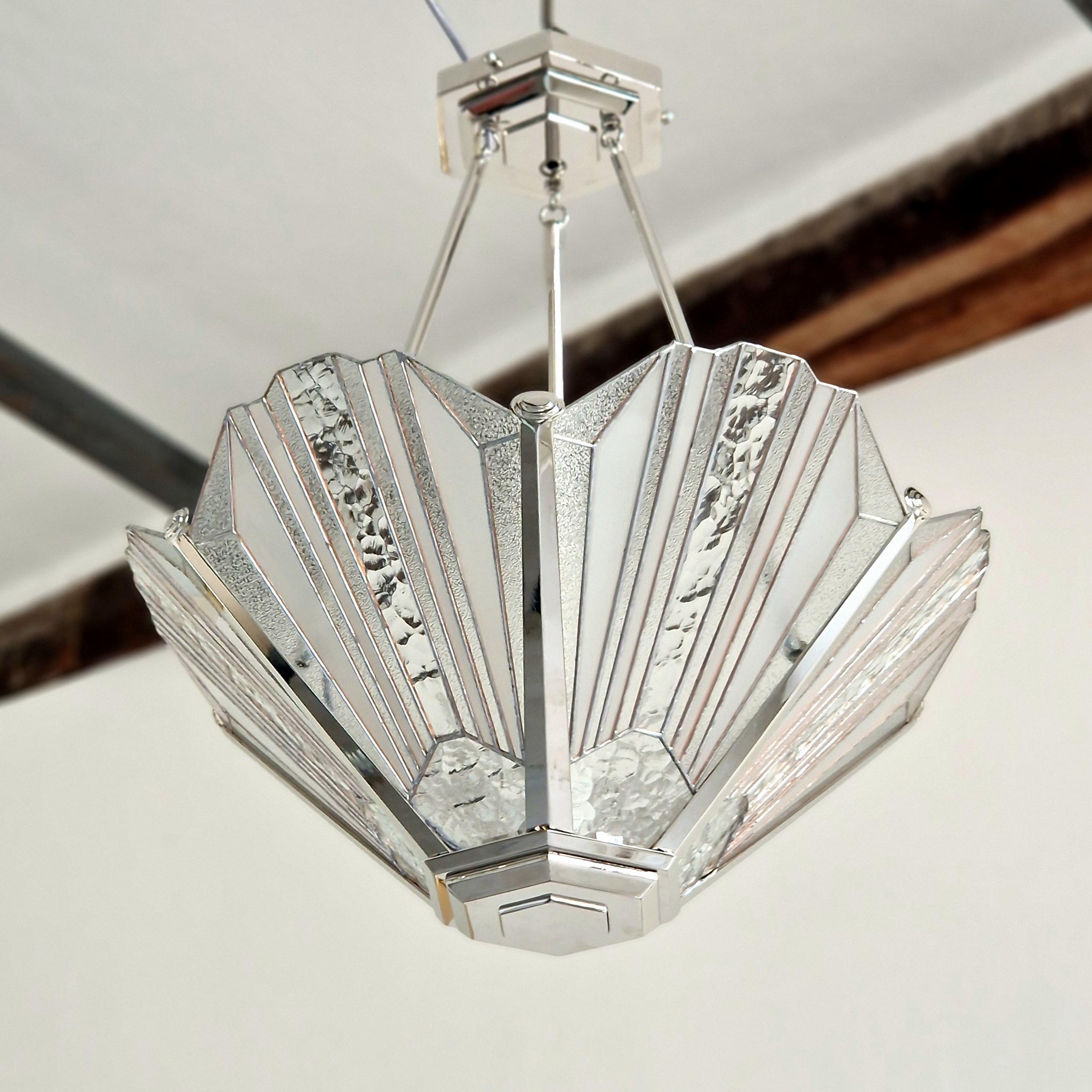 
An Art Deco chandelier in bronze with elegant lines, blending robustness and refinement. It features textured stained glass, arranged in perfect symmetry. The 1920s-inspired motifs create a unique play of light, evoking a warm and sophisticated