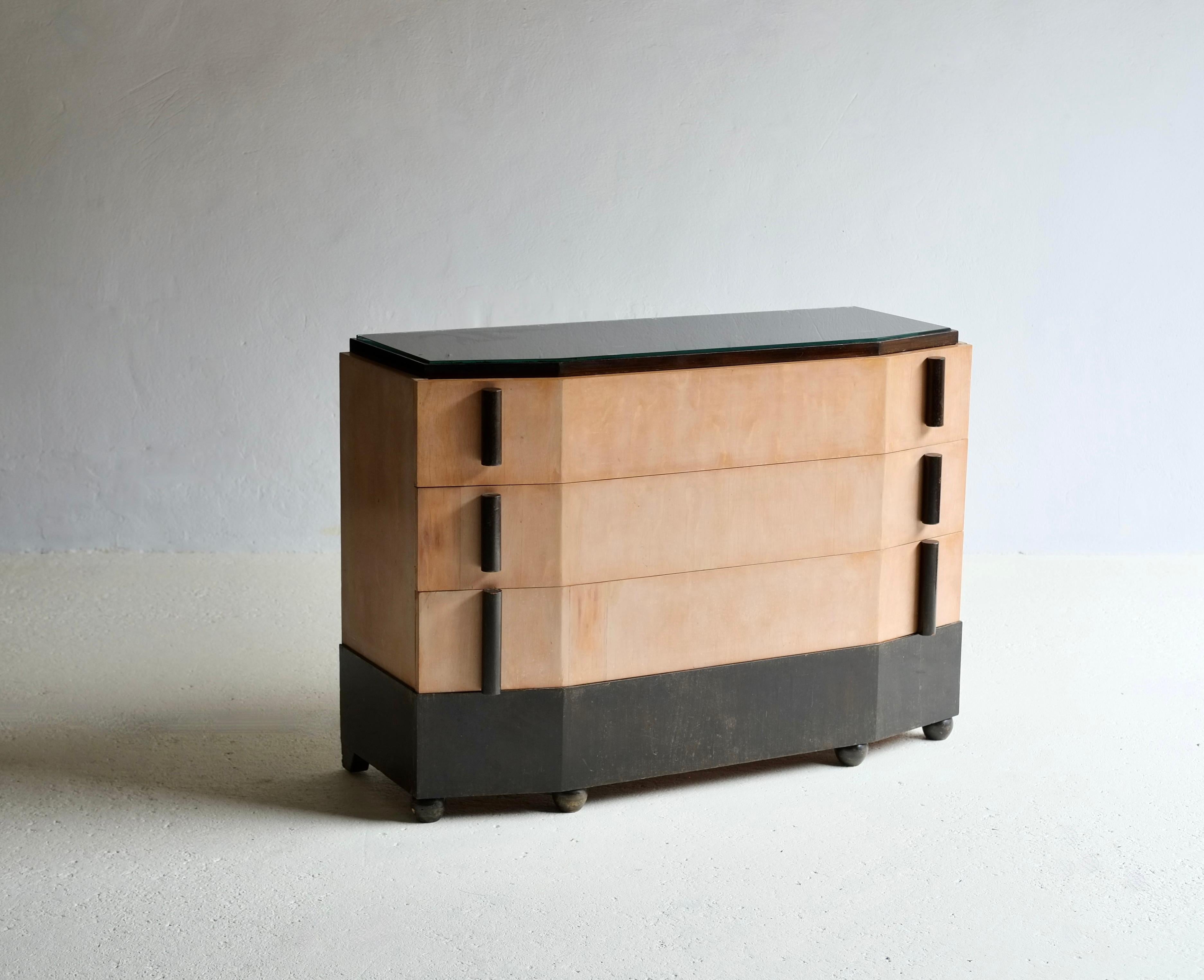 Un'elegante cassettiera francese in stile Art Déco.

Circa 1930 - anni '50. 

Tre cassetti impiallacciati in legno con maniglie cilindriche e un cassetto inferiore ebanizzato sollevato su piedi sferici. Piano in vetro nero. 

Piccole riparazioni
