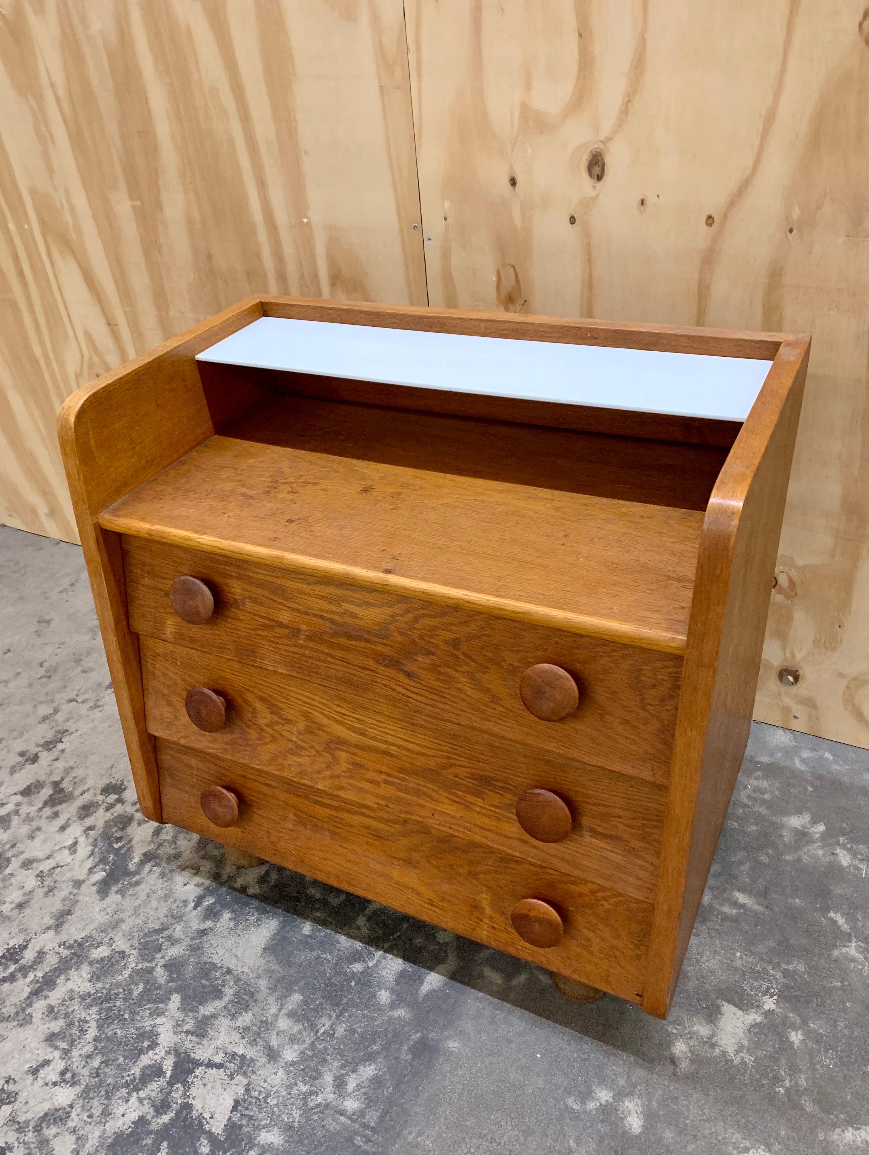 Kleine schicke französische Art Deco Kommode mit 3 Schubladen und einem in das Eichenholz eingelassenen weißen Opalglasboden. Schöne klobige Griffe und die Kommode hat eine Höhe, die es ideal als Nachttisch als auch macht. 2 kleine Kerben auf dem