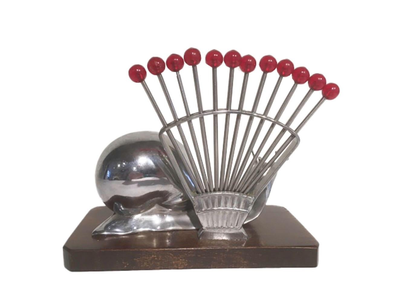 Vintage French cocktail pick set, having 12 forked picks with red Bakelite ball tops in a fan-shaped chrome holder behind a large chrome snail, all set on a mahogany base. The forked picks are equally useful for cocktail garnish or hors d' oeuvres.