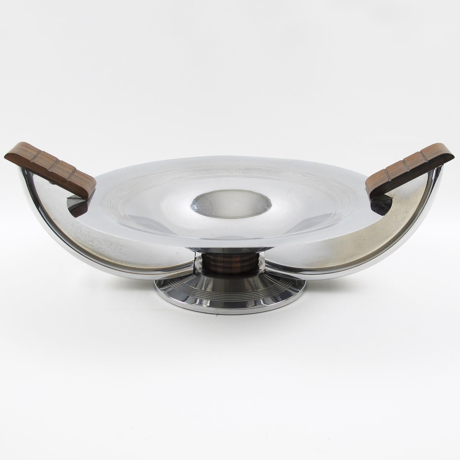 This stylish Art Deco centerpiece or decorative bowl was hand-crafted by French silversmith Massabova, Paris, in the 1930s. The round geometric shape has wing handles. The chrome-plated metal body is ornate with carved Macassar wood and complemented