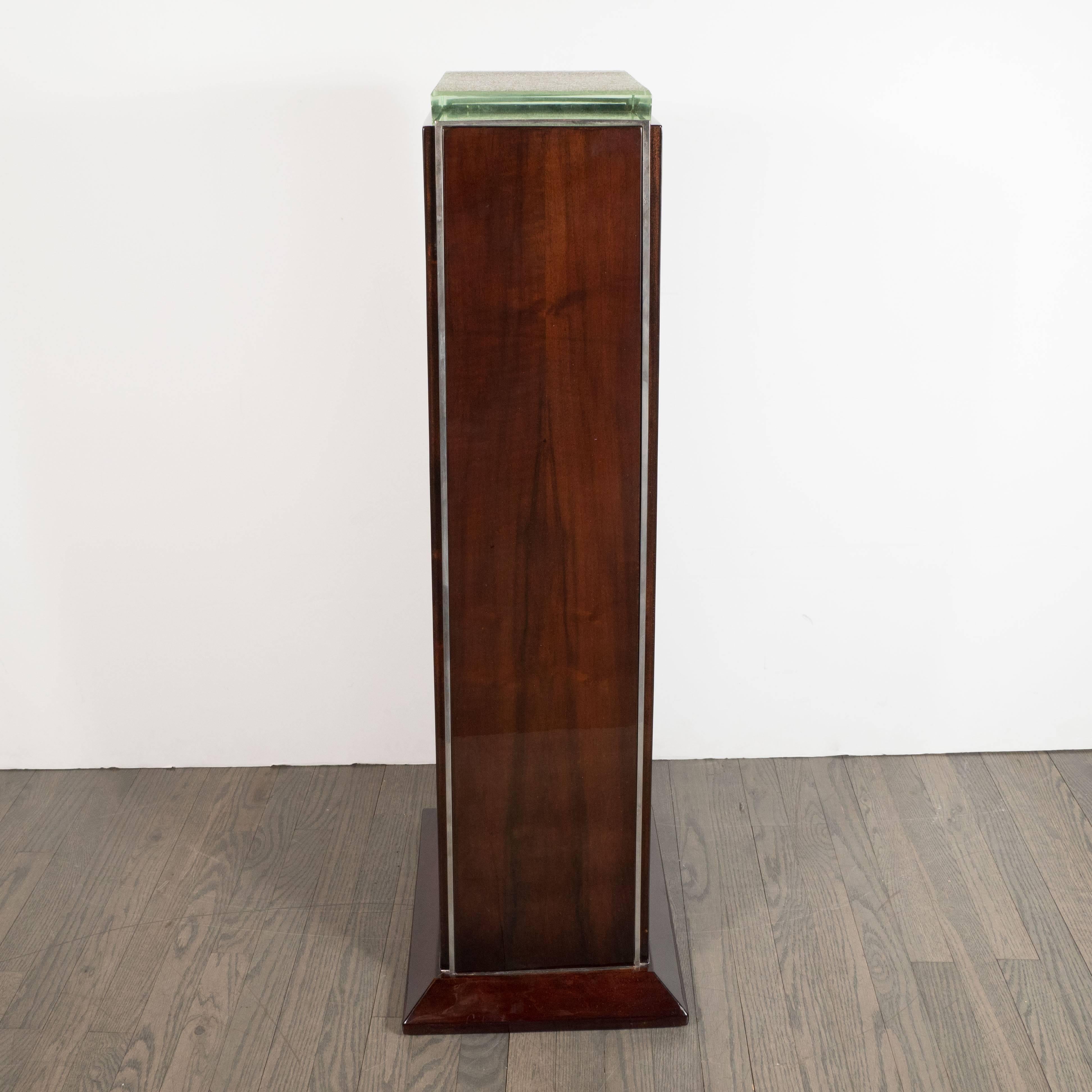 This elegant skyscraper pedestal was realized in France, circa 1930. With its austere subtly tapered plinth form composed of book matched mahogany with chrome detailing, it represents a stunning example of the time and place. The rectangular base