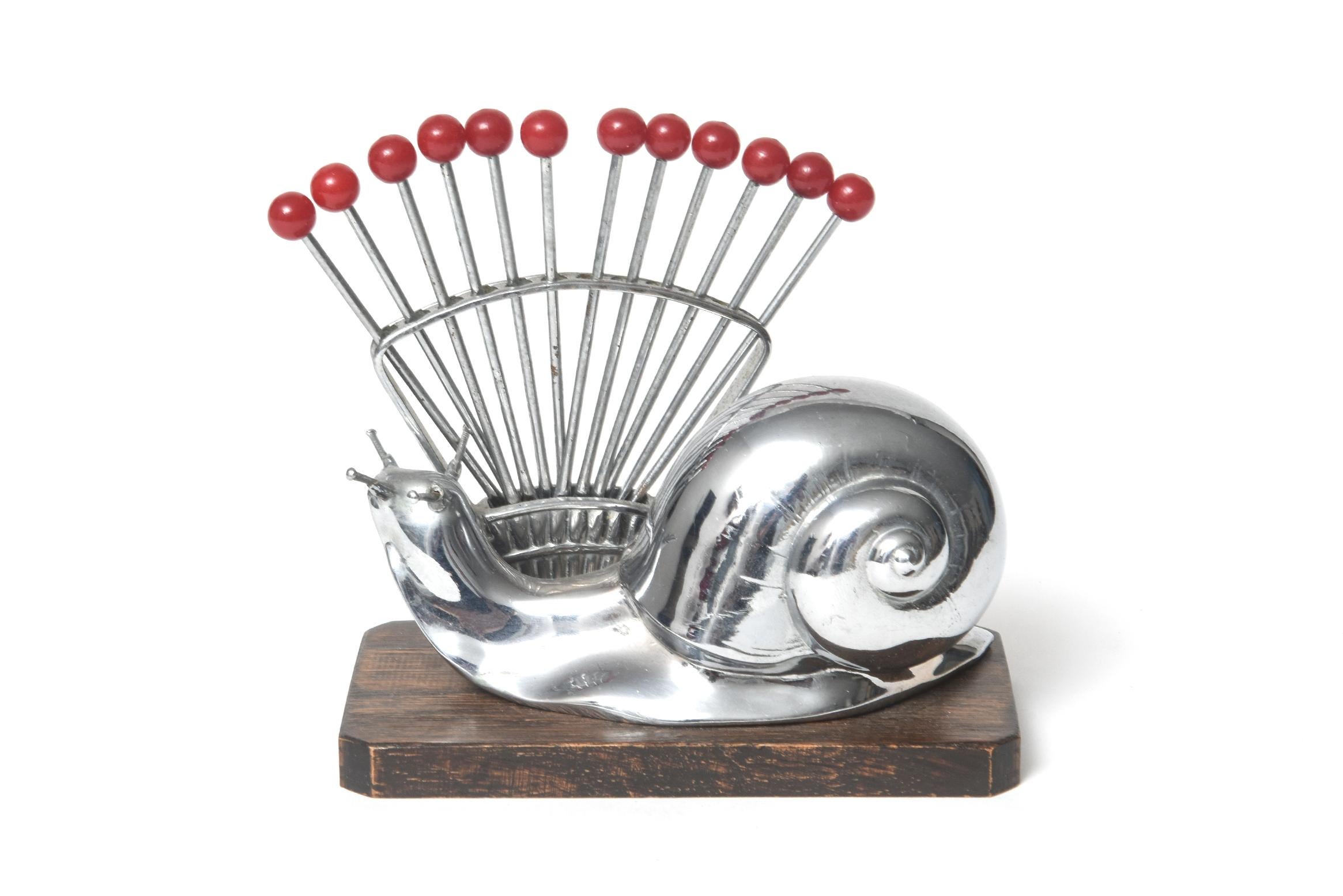 A French Art Deco cocktail pick set featuring a large chrome snail set on a mahogany base. The design is by the famed French Art Deco illustrator Benjamin Rabier, who had a side job designing entertaining barware. The twelve picks fan out behind the