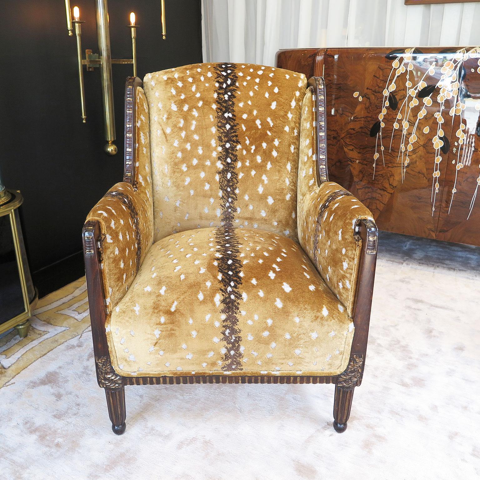 French Art Deco chairs with a Classic wingback style. The frame is in a dark stained maple wood with linear ribbed gold leaf carvings along the arms and lower frame. An intricate floral carving sit above the upper front legs done in gold leaf. The