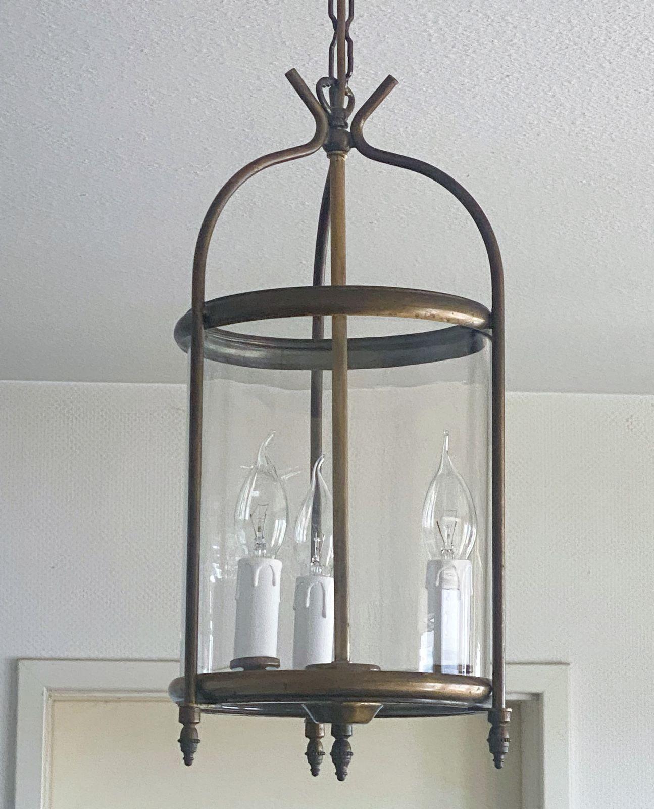 Elegant Art Deco cylindrical clear glass lantern, France, 1920-1929. Mounts of old bronze with a central three-light candelabra cluster.
In fine vintage condition, beautiful aged patina to bronze, rewired.
Three E-14 light candle bulb