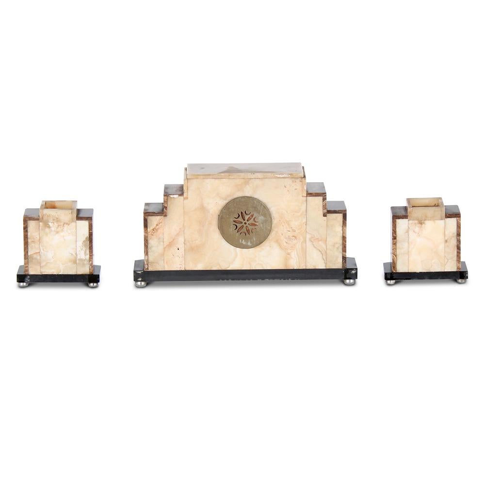 A French Art Deco period three-piece garniture set, the clock with rectangular face and stylised geometric numerals set against a textured metal dial all set within a geometric case of onyx with nickel-plated metal on a black marble base. Decorative