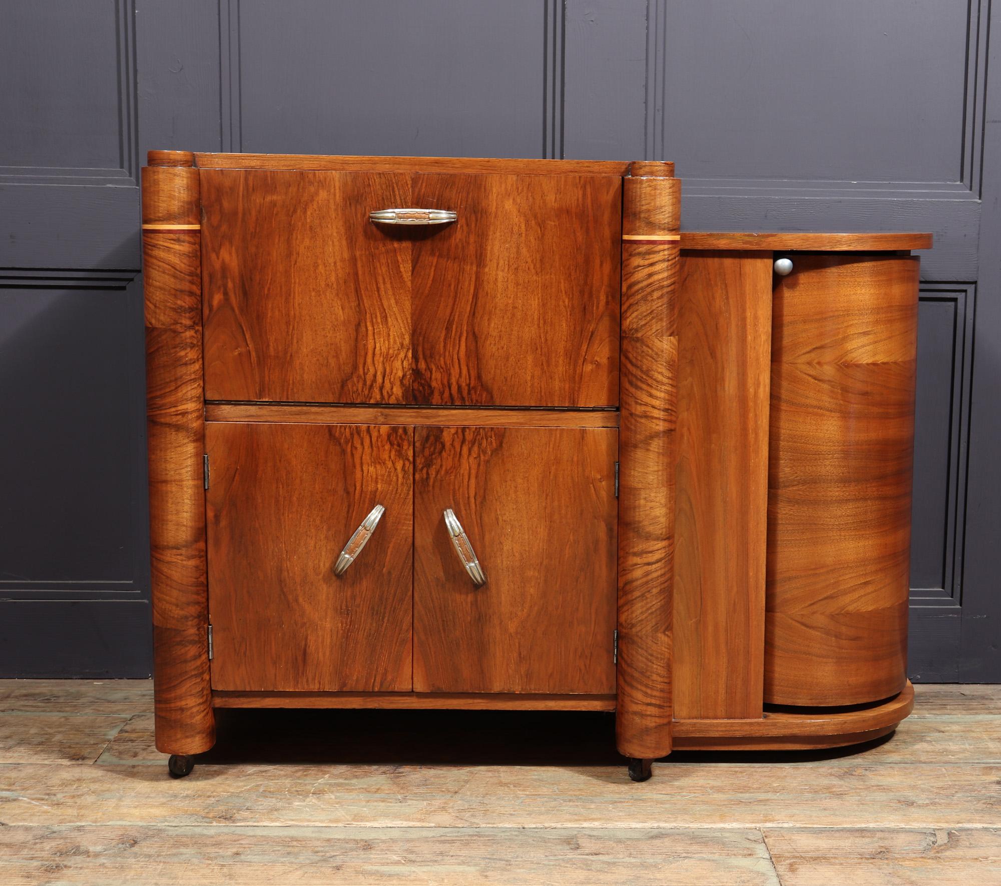 A small French Art Deco cocktail cabinet produced in the 1940’s in walnut with a fall down top section with mirrored drinks making area, below is cupboard for bottles an to the right is a cylindrical roll round bottle holder section, the cabinet has