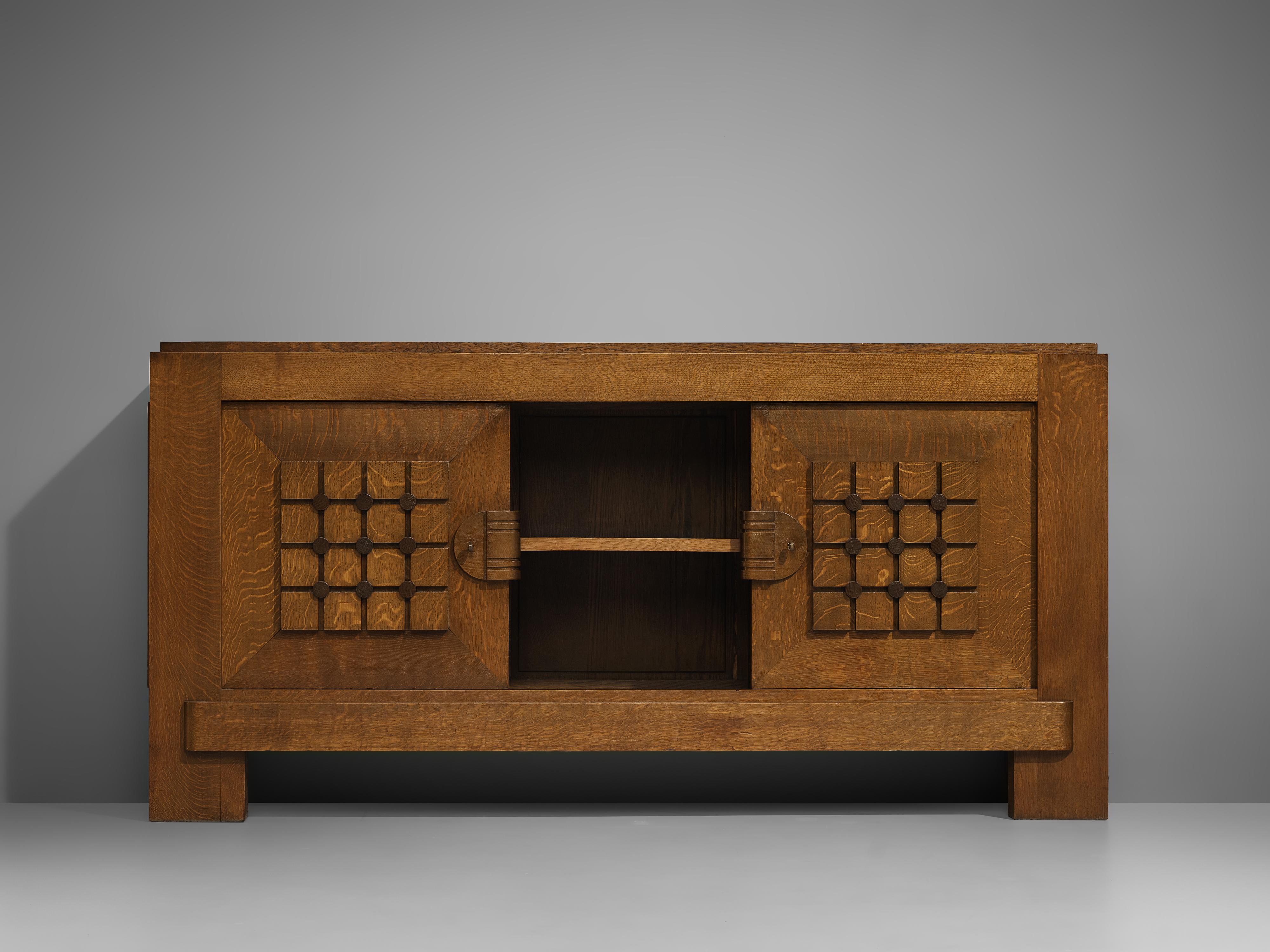 Credenza, stained oak, France, 1940s 

Sturdy sideboard in oak with graphical door panels. The sideboard is equipped with several shelves behind two doors. The square structure on the front gives this cabinet a vibrant appearance and emphasize the