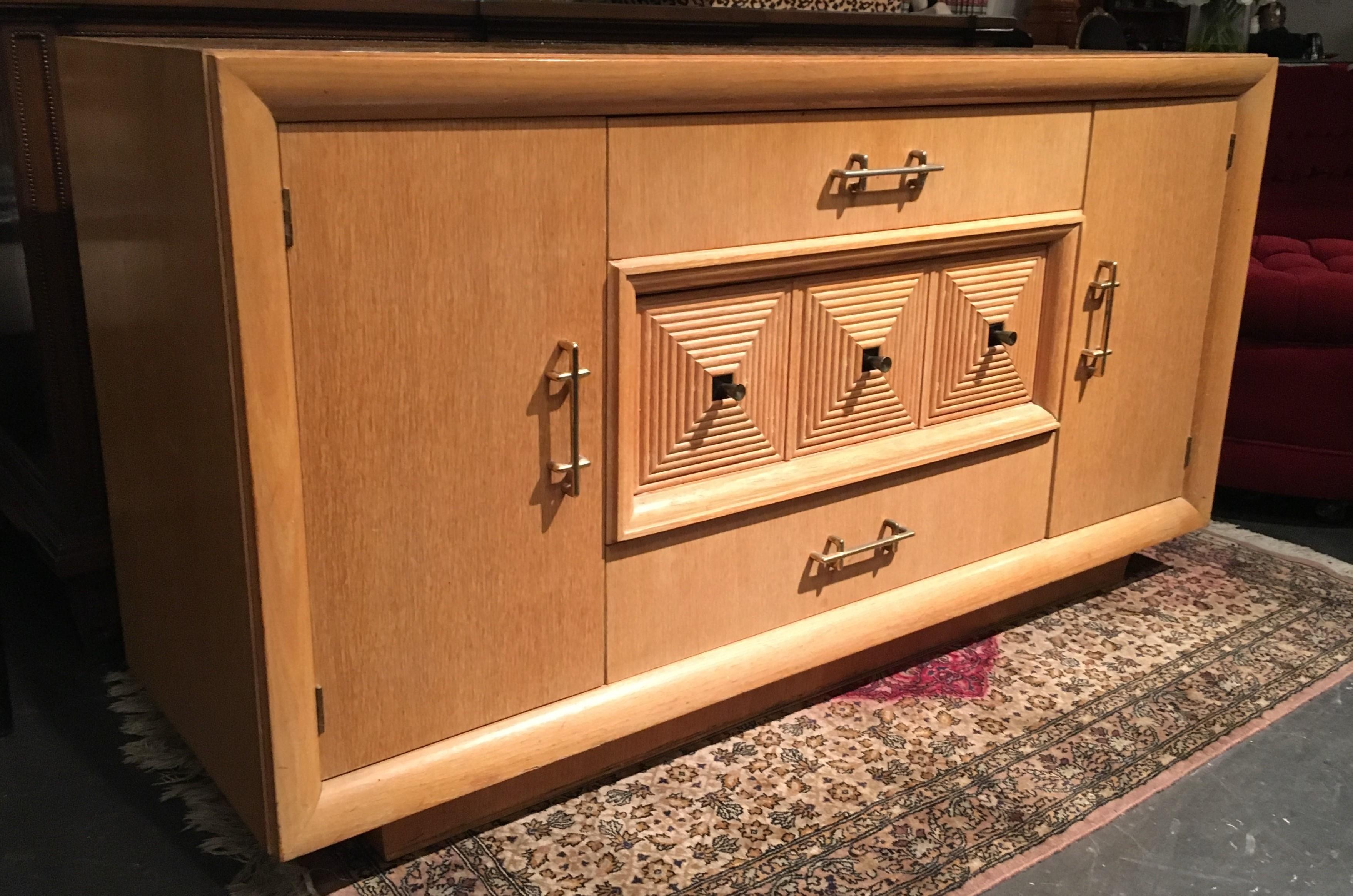 Beautiful French Art Deco 1940s cerused oak credenza or sideboard. Centered is a three-drawer unit flanked by two cabinet doors with open storage, resting on a plinth base. The middle drawer decorated with multiple square elements with brass