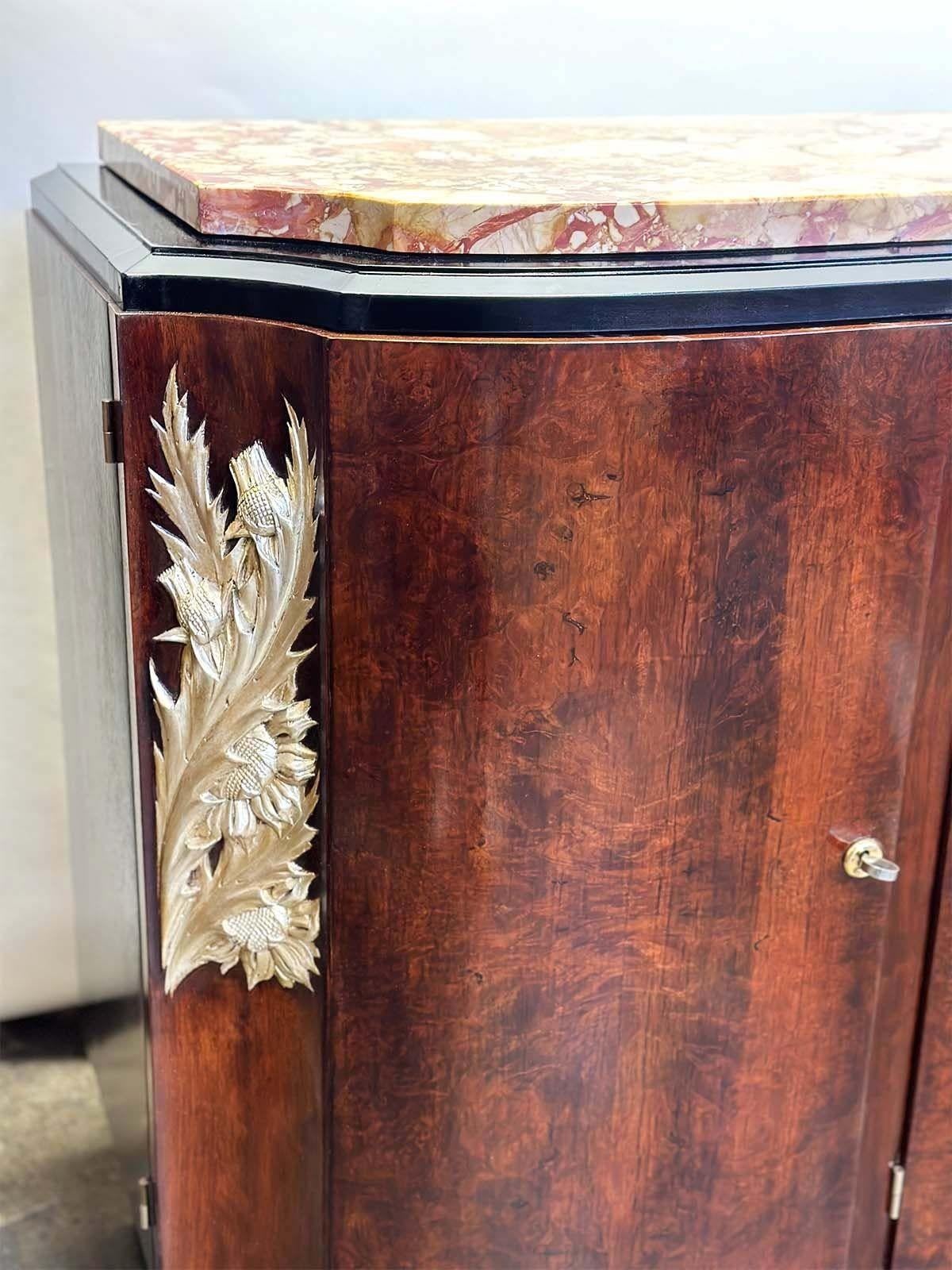 La crédence française en bois Art déco des années 1920 est un meuble exquis qui incarne l'élégance et la sophistication du mouvement Art déco. Il se caractérise par un design épuré, alliant matériaux luxueux et sculptures botaniques. La crédence est