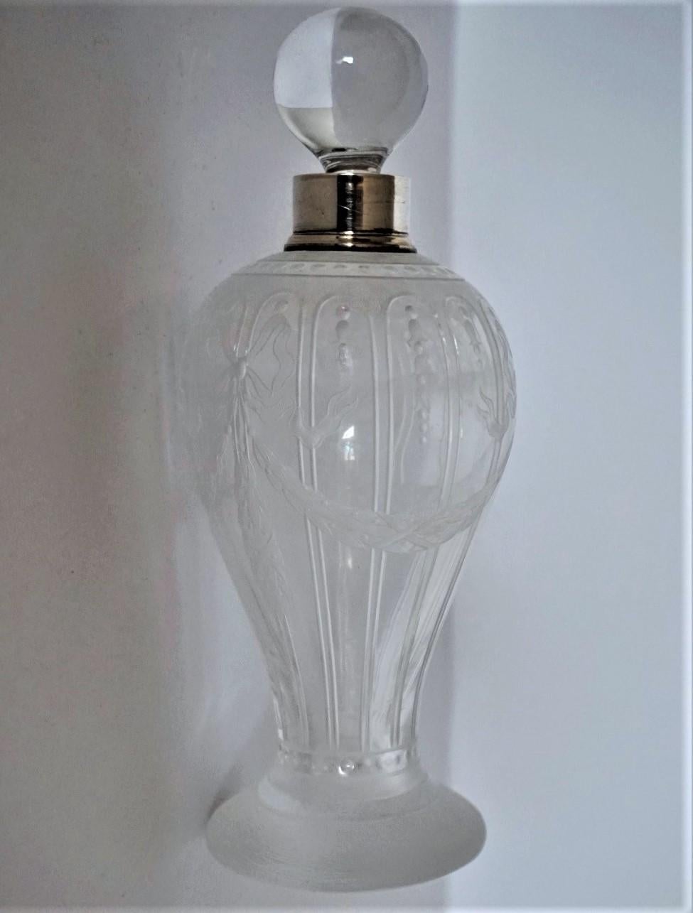 Large Art Deco clear and frosted crystal glass perfume bottle, beautifully high relief engraved with elegant motifs, wreaths and bows, France, 1920-1929. Neck with sterling silver mount, clear crystal glass sphere stopper.
Measures: Height 7.50