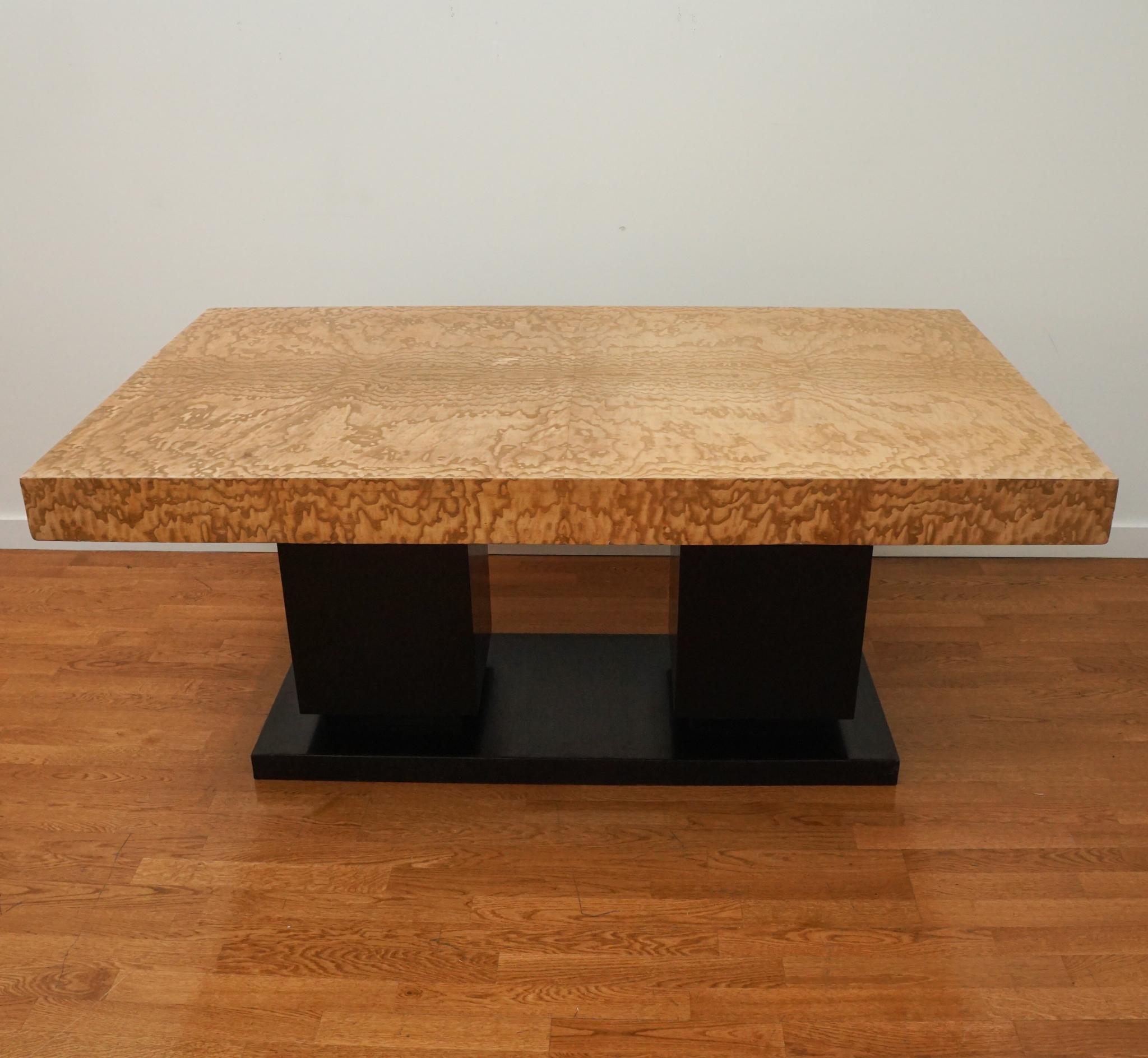 Cette exquise table de salle à manger Art déco, originaire de France et datant des années 1930, présente un plateau en ronce de frêne soutenu par deux socles carrés reposant sur une base rectangulaire surélevée. La table a des feuilles de 28