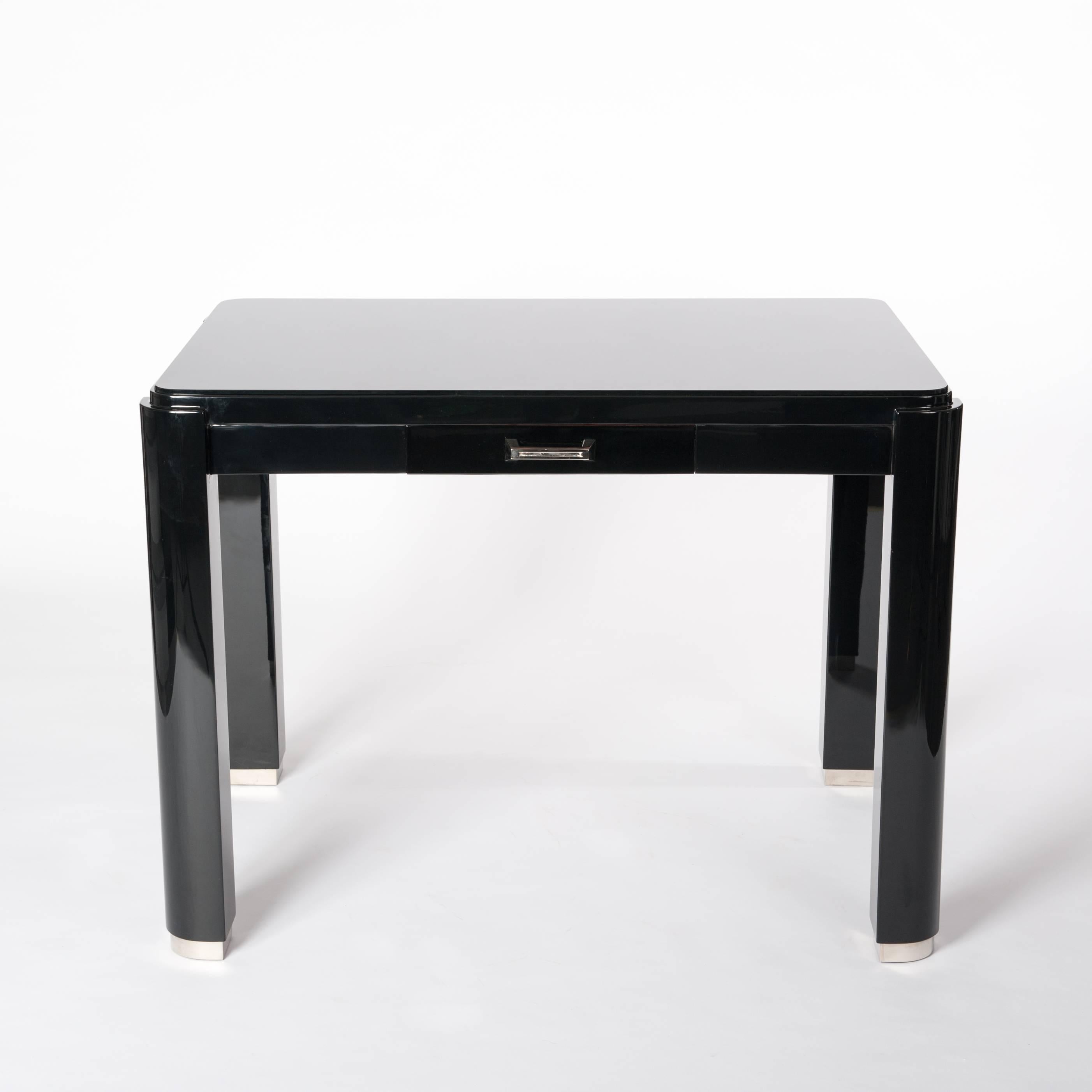 Small French Art Déco wrtiing table or desk in cubistic design.
Black lacquered with re-nickeled handle and foot mountings.
The tabletop is covered by a black glass plate for protecting the surface.

