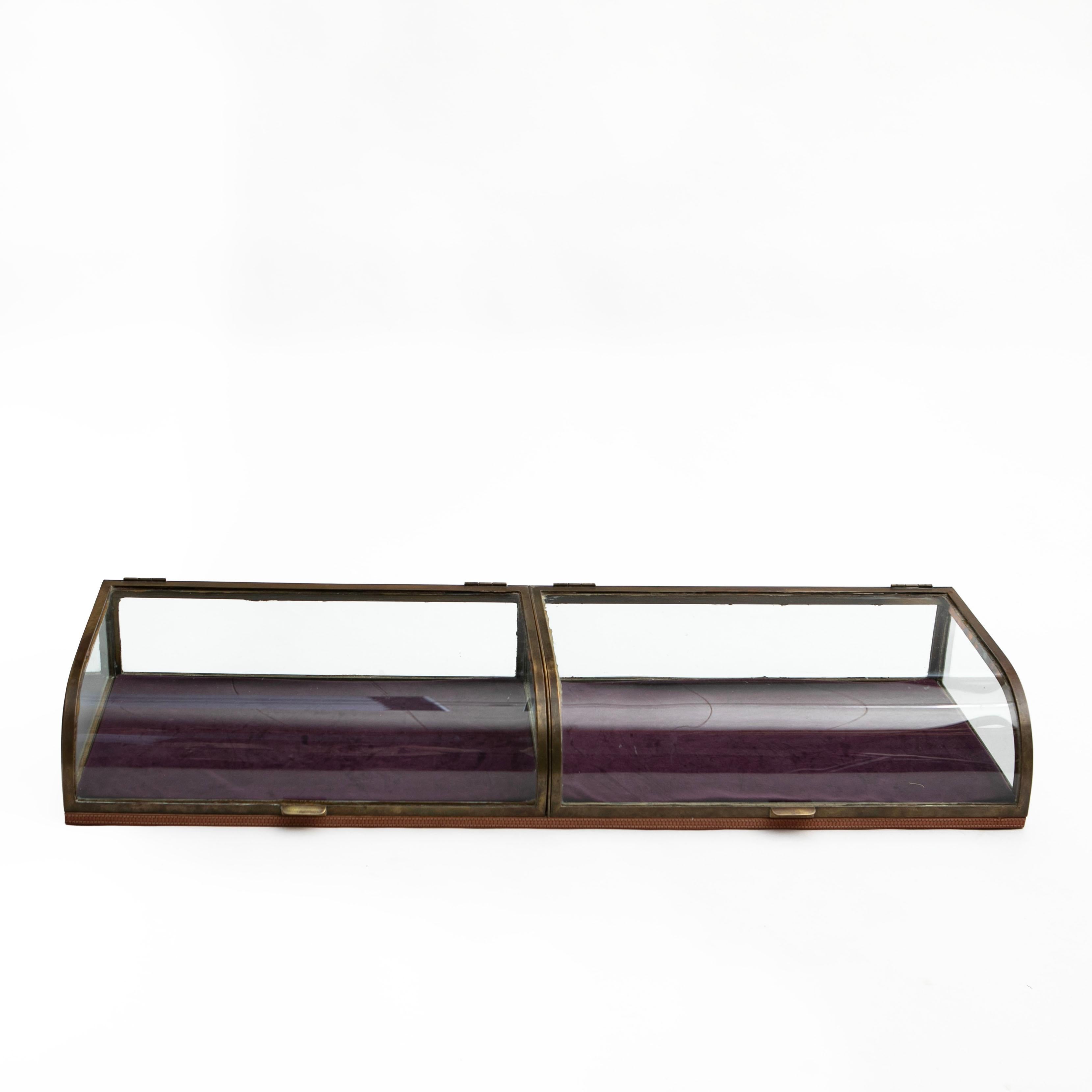 French antique curved glass countertop showcase made of glass and quality brass.
Brass frame with two classic curved glass door and glass sides. The bottom is covered with purple velour (this can be easily replaced).
In untouched good condition with