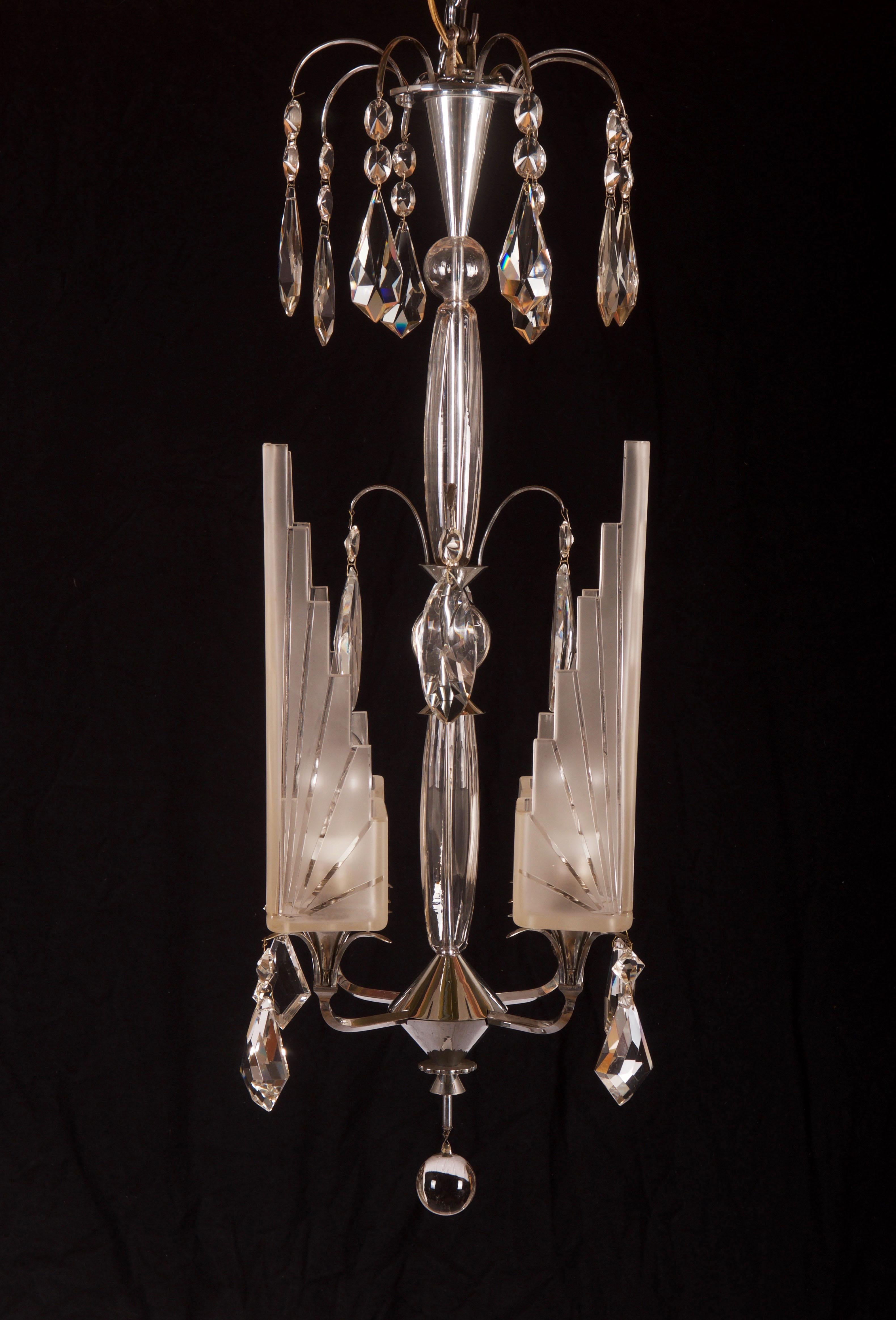 Schöner französischer Art-Déco-Kronleuchter aus den 1920er Jahren mit vier Lichtarmen mit Schirmen aus Milchglas mit Strahlenschleifern, Stiel und Prismen aus Glas, Rahmen und Oberteil aus vernickeltem Metall. Eines der Gläser hat einen kleinen