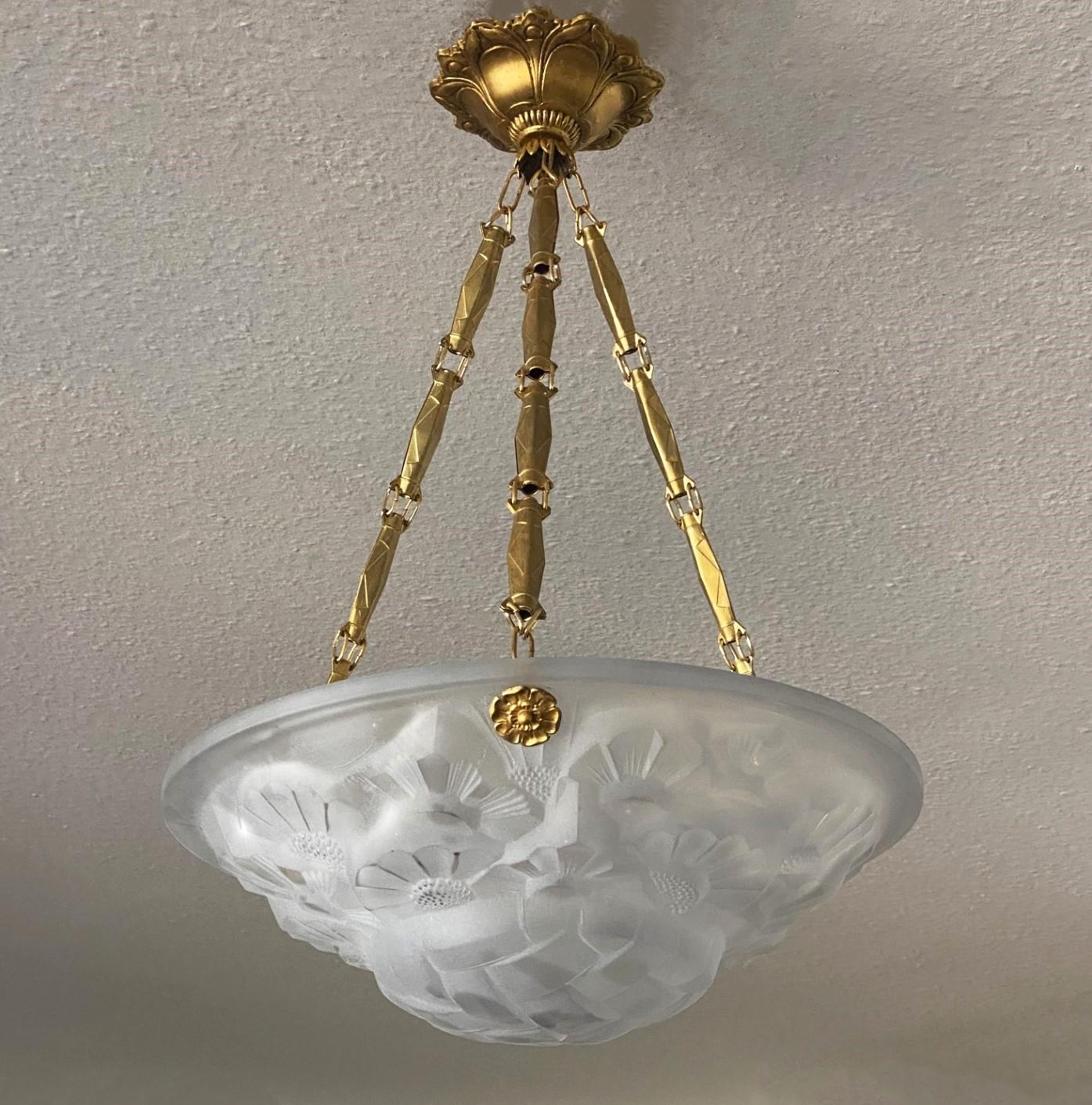 Arte Deco Glass and gilt brass pendant by Degué, France, 1930s. White frosted glass shade with beautiful Arte Deco floral and geometrical motifs supported by three tipical Art Deco brass chains conneting to a beautiful gilt brass canopy. Signed