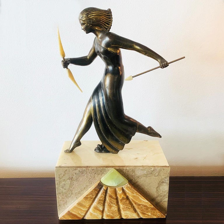 Art Deco lamp depicting Diana the Huntress running with bow and spear, both in carved bone, on multicolored Marbles and illuminated from pedestal below via an Alabaster top “window”. The front of the pedestal has a pyramid of brown Marble with