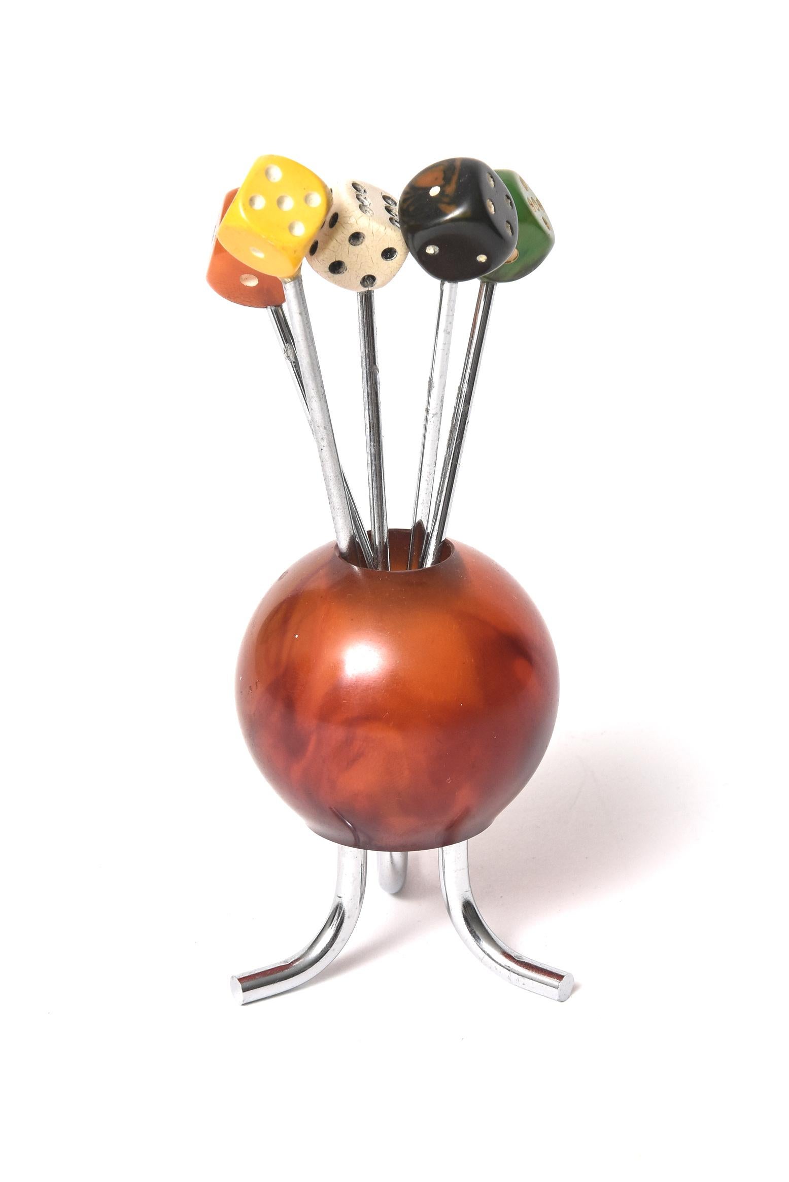 A French Art Deco cocktail pick set featuring an amber colored bakelite ball on 3 chrome legs holding 5 dice cocktail fork picks. The dice are wood and bakelite with a chrome fork pick stick These cocktail pick holders (