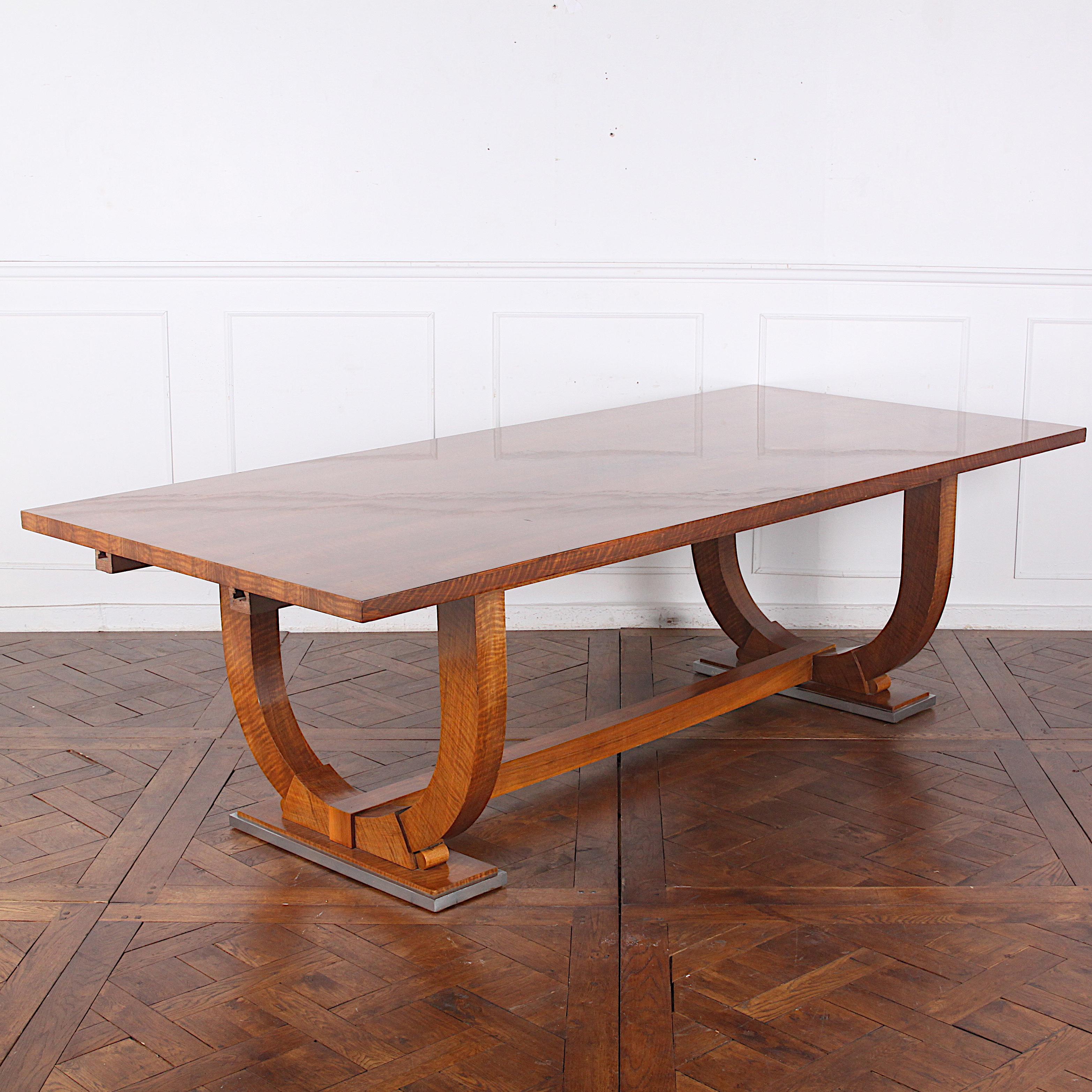 An important French Art Deco period walnut dining table by Parisian designer ‘Jules Leleu’. The simple rectangular plane of the top slab is veneered in figured bookmatched walnut and is supported on two bold U-shaped ends, each resting on a